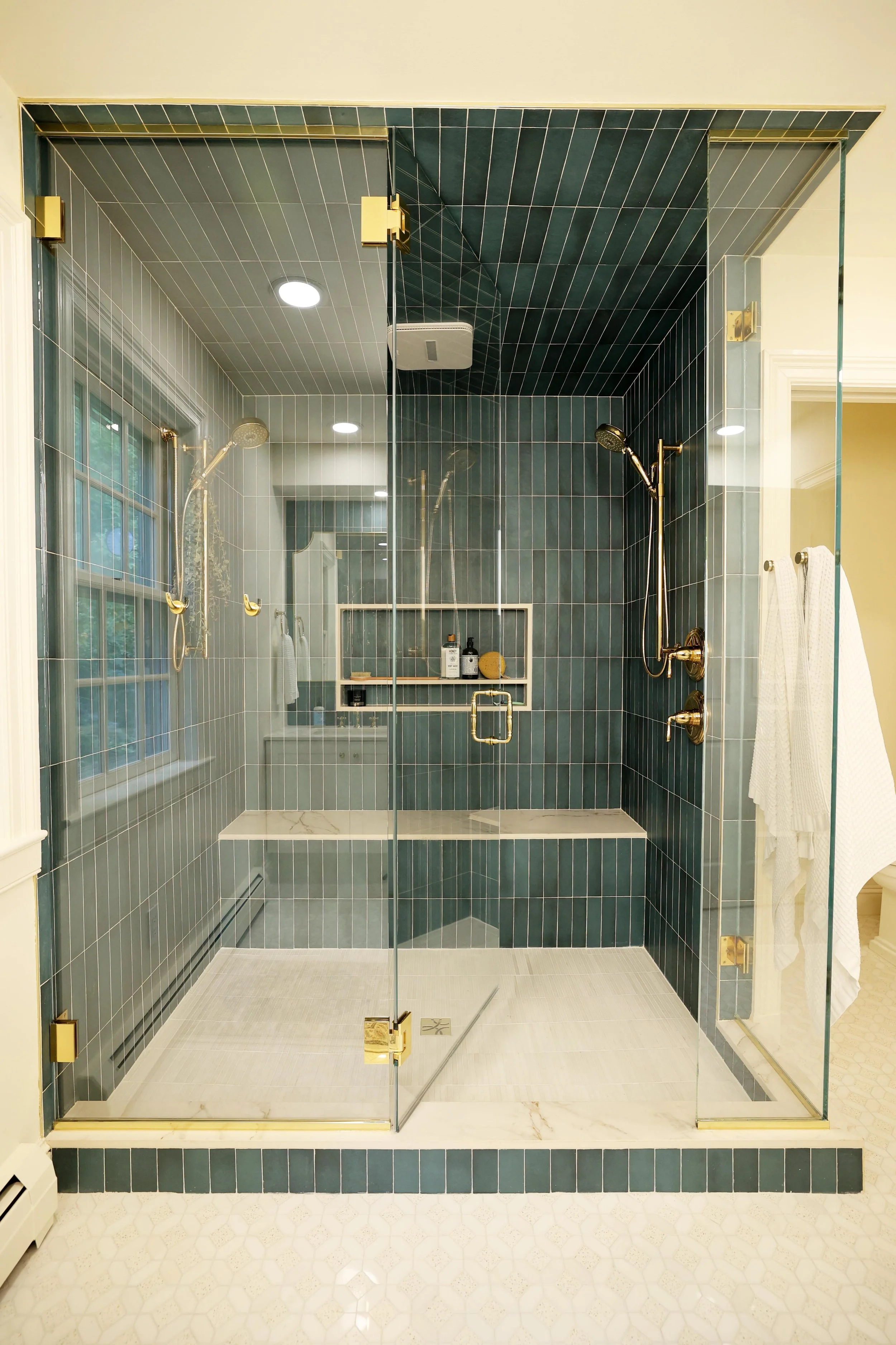 Glass enclosed shower with deep blue vertical tile and brass fixtures in primary bathroom renovation