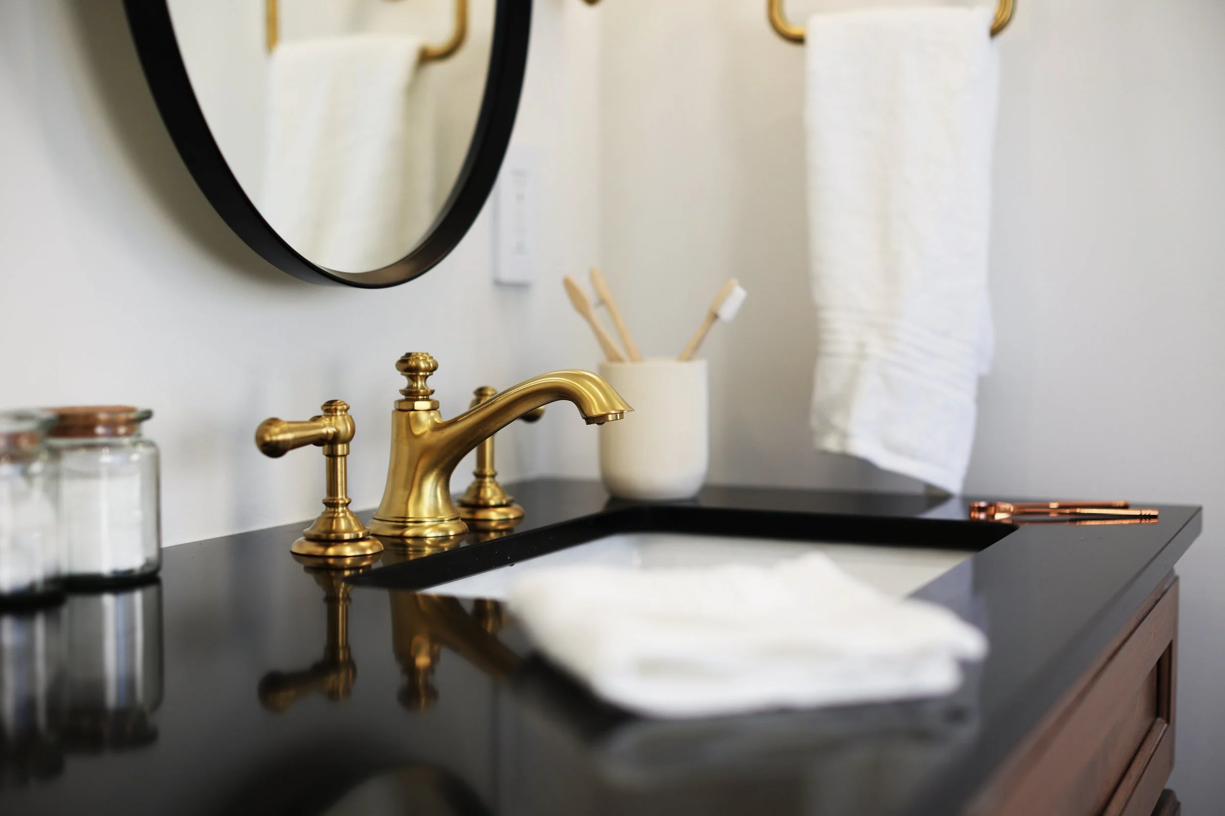 Bathroom vanity with black countertop and brass faucet in an elegant black and brass bath.