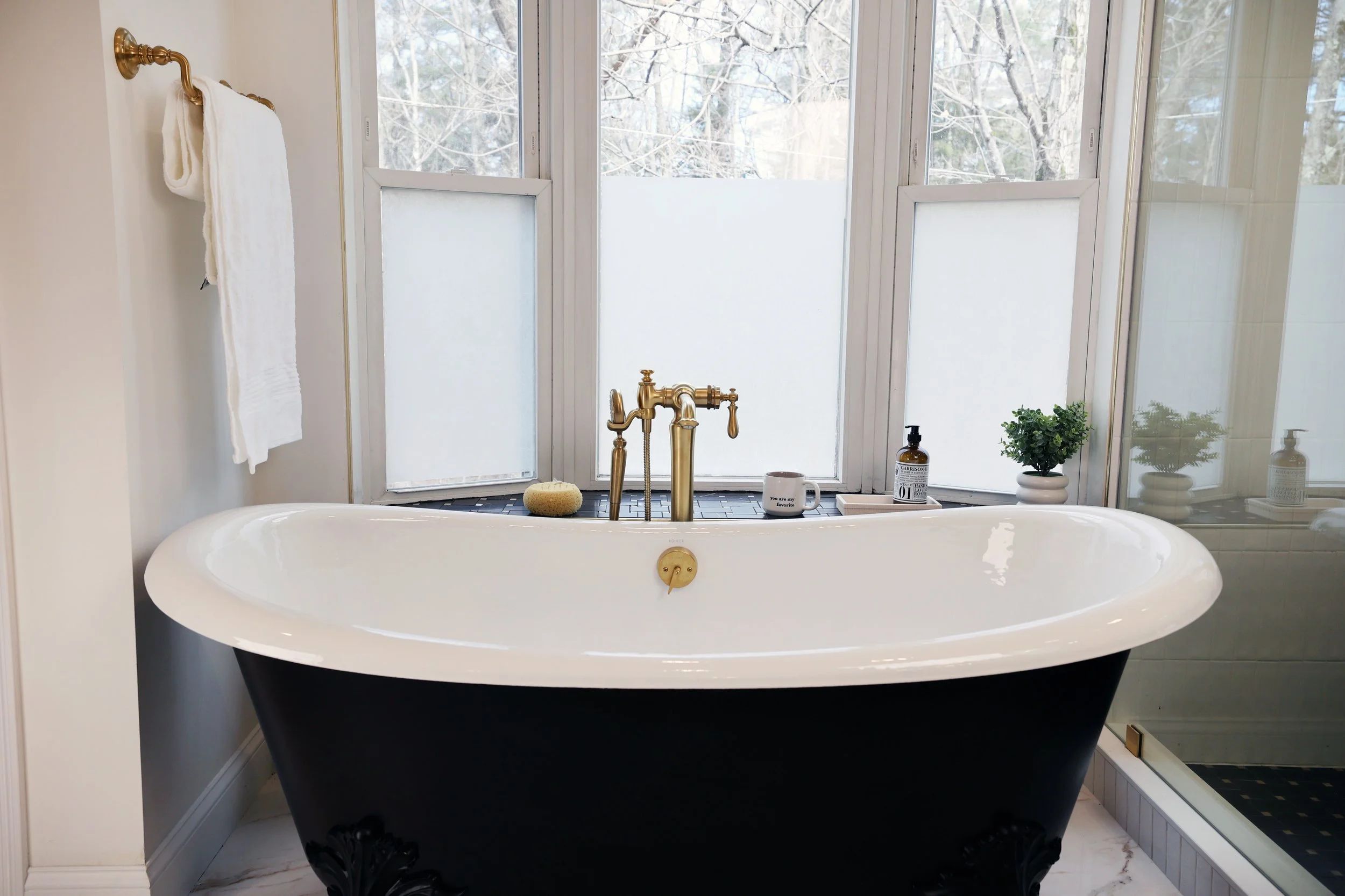 Freestanding claw foot tub by Kohler beneath windows in a historic Victorian bathroom renovation in Bethlehem New Hampshire.