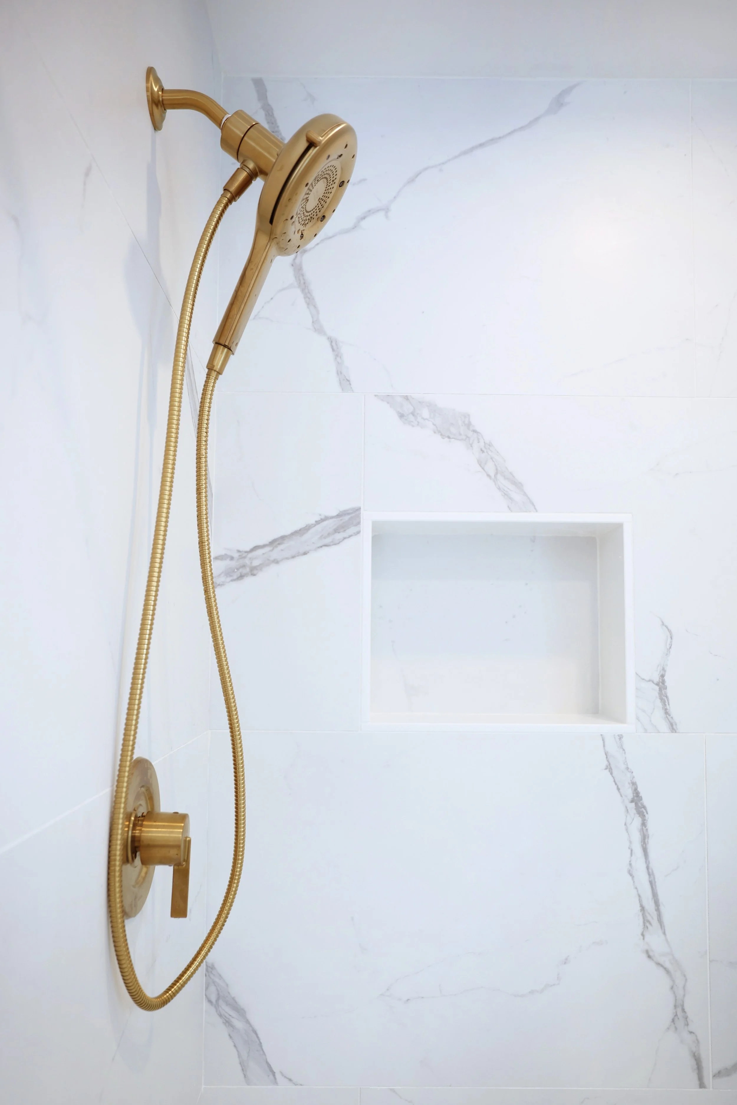 Brass handheld shower fixture from the Moen Cia collection mounted on marble tile.