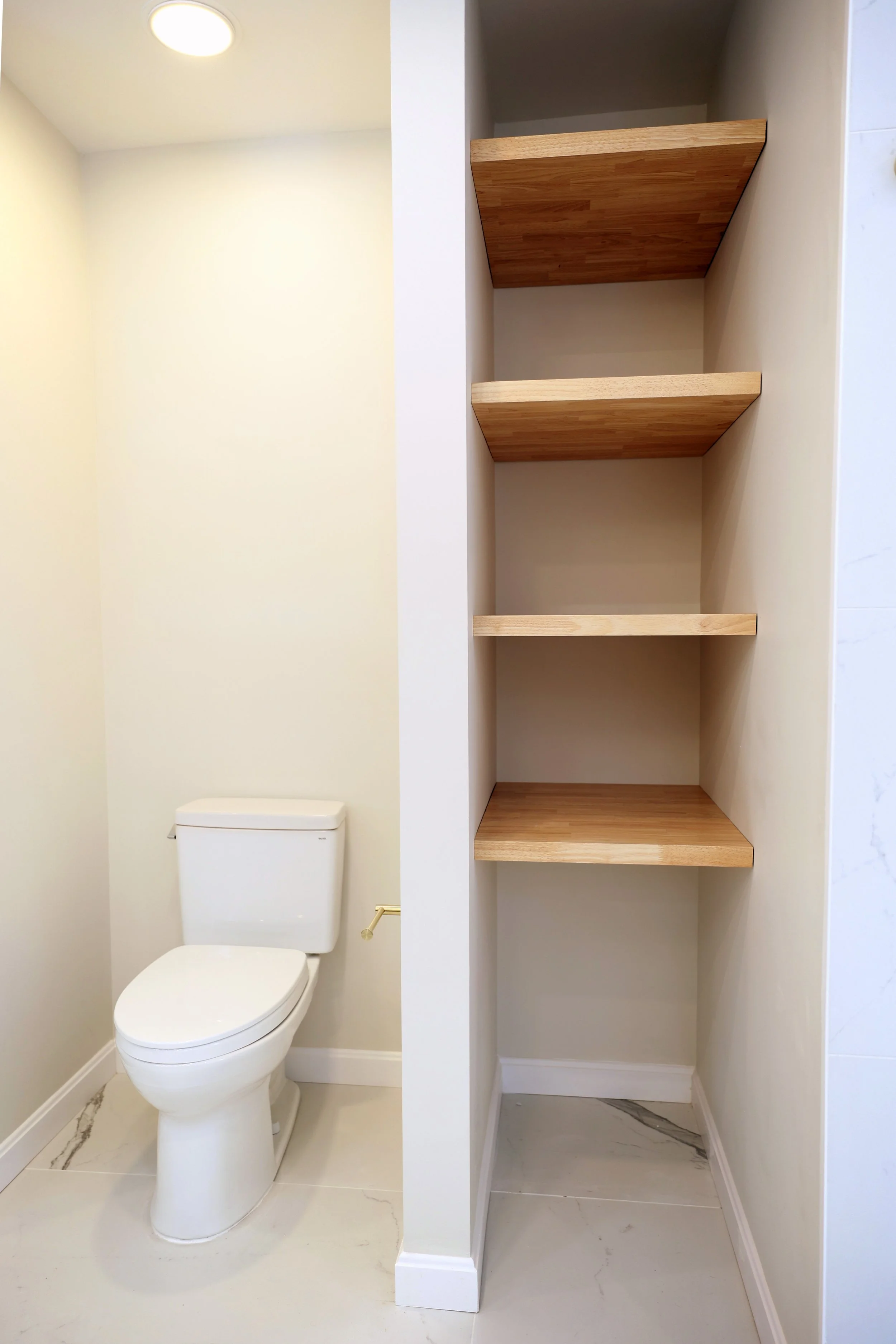 Toilet alcove with built-in wood shelving in a primary bathroom in the Upper Valley.