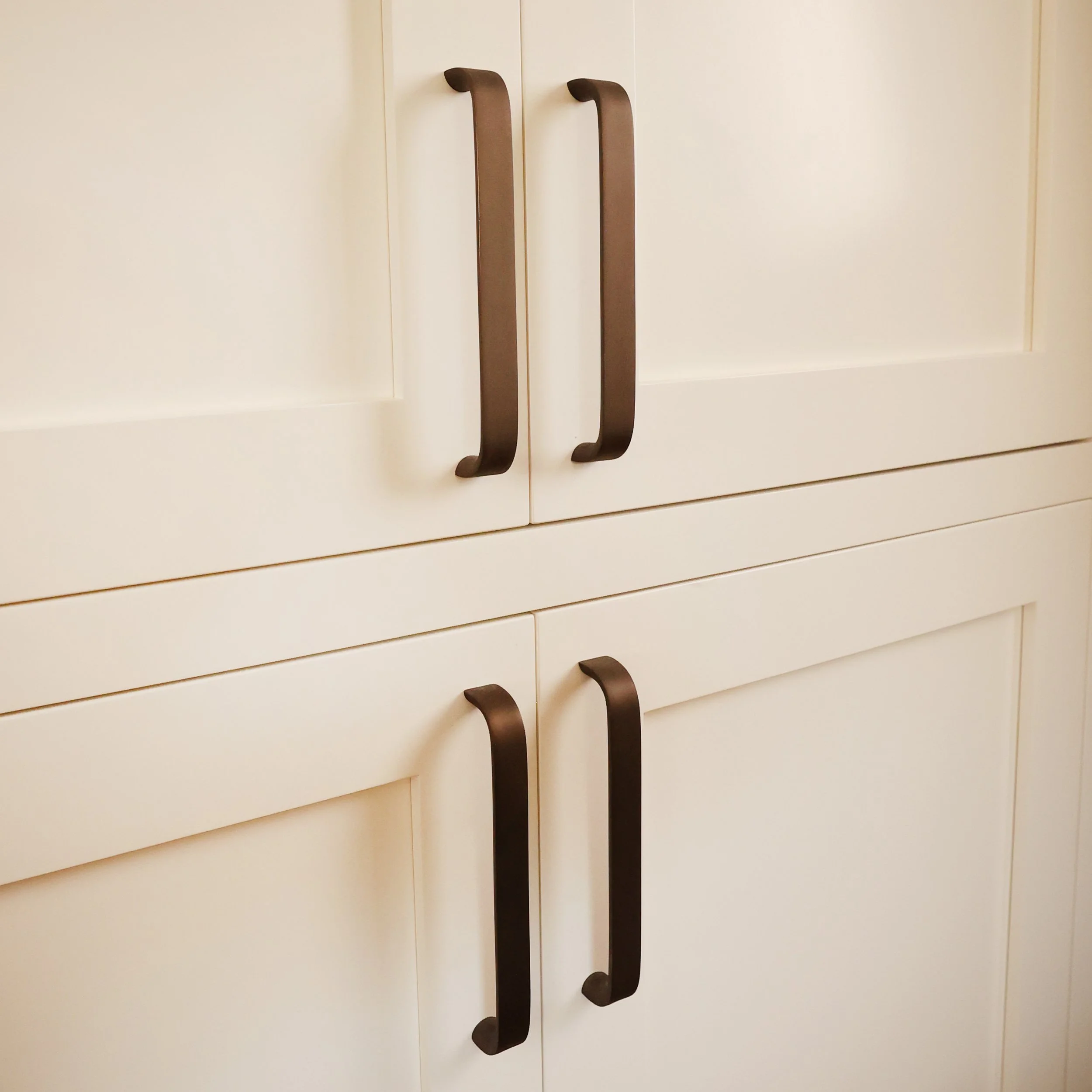 Oil-rubbed bronze cabinet pulls on tall cream pantry doors in a historic Bethlehem NH farmhouse kitchen.