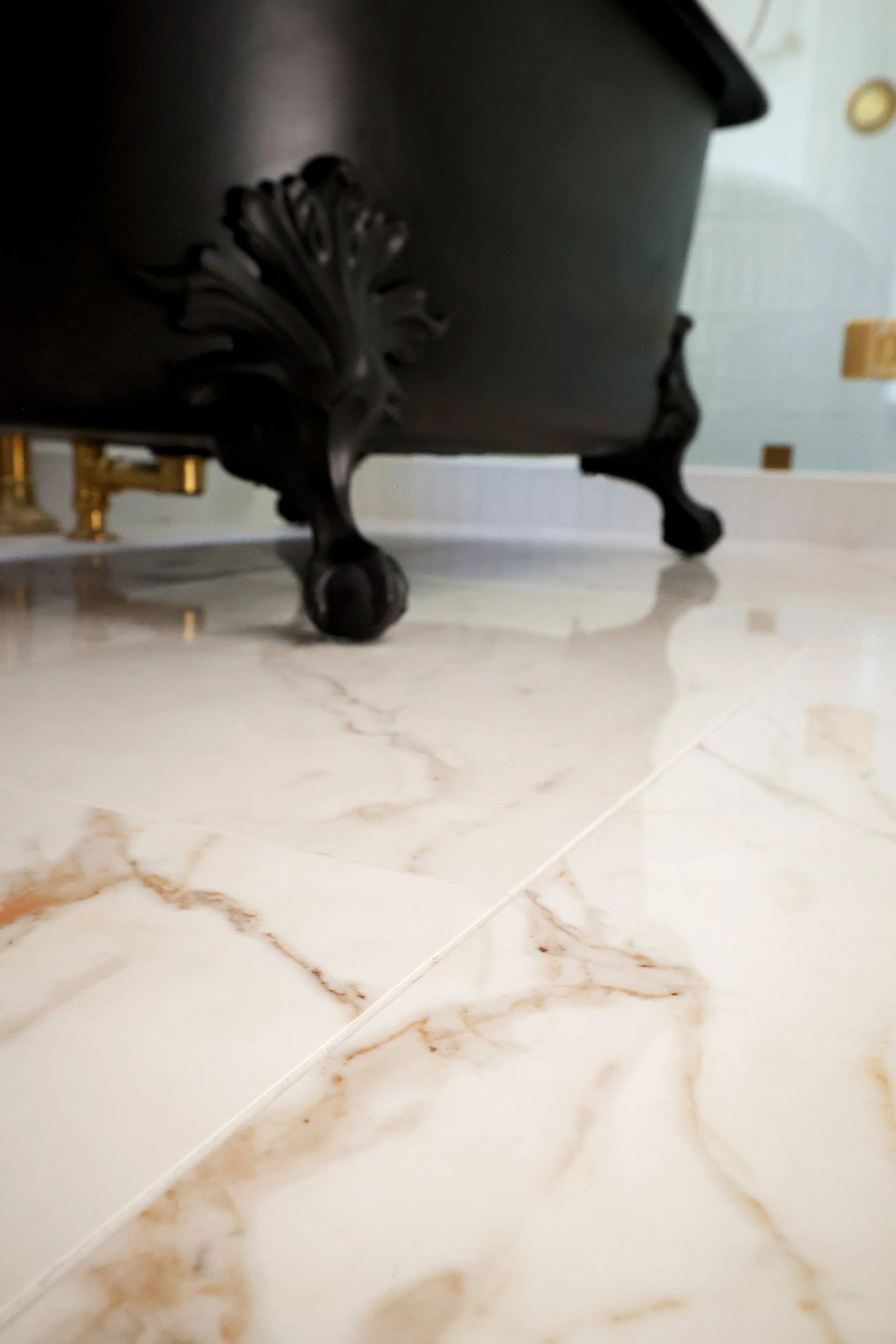 Decorative black clawfoot tub leg on warm calacatta gold marble tile floors in a historic Victorian bathroom in Bethlehem NH.