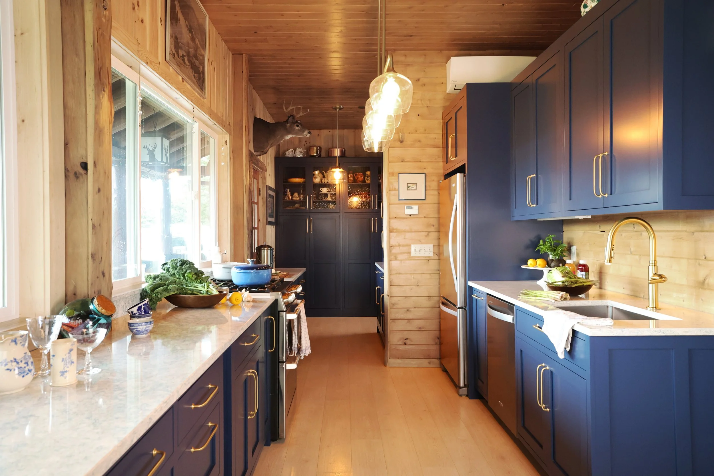 Galley style lodge kitchen with Navy Blule Crown Point Cabinetry and wood walls in a New Hampshire retreat.