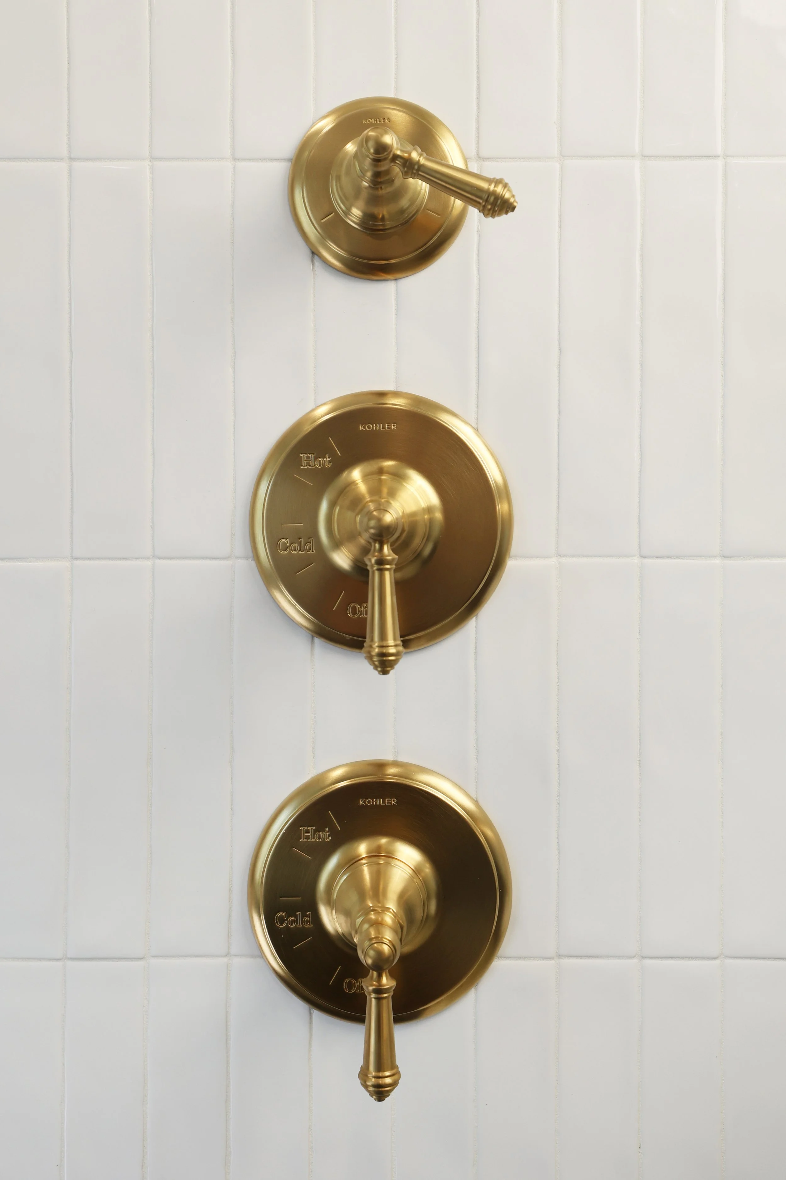 Polished brass shower controls mounted on white vertical tile in a classic Victorian bath.