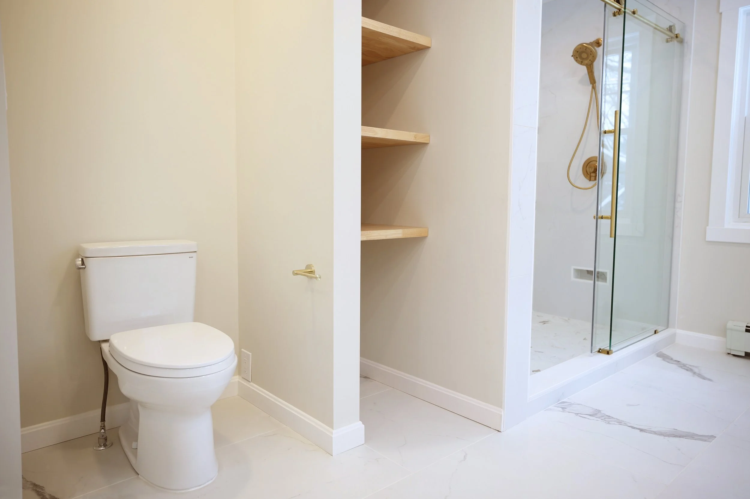 Toilet alcove and view toward glass shower entry with marble-look tile within a primary bathroom renovation in Lebanon New Hampshire.