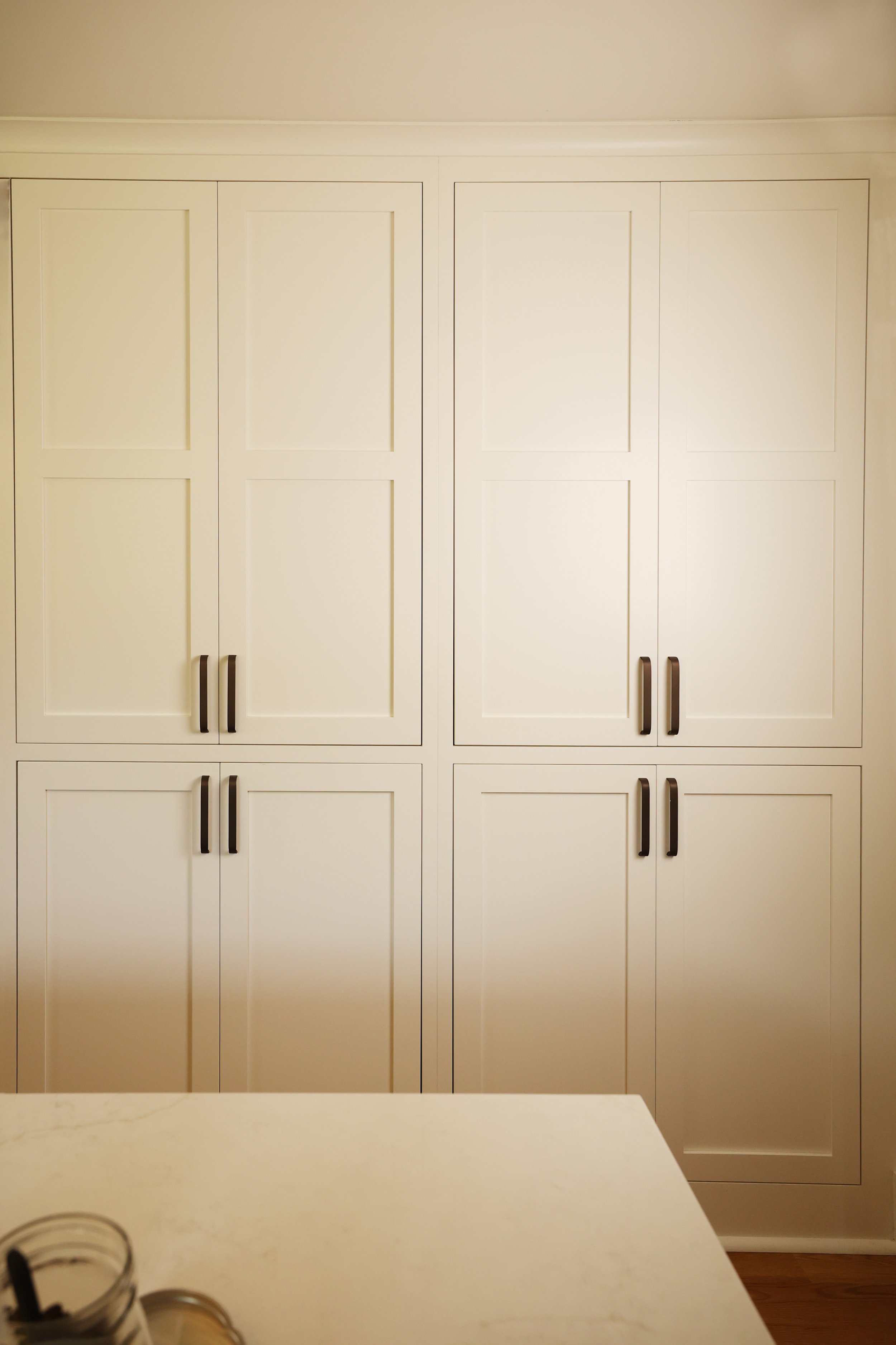 Full pantry cabinet wall in painted cream with dark pulls in a pre-1900 farmhouse kitchen renovation.