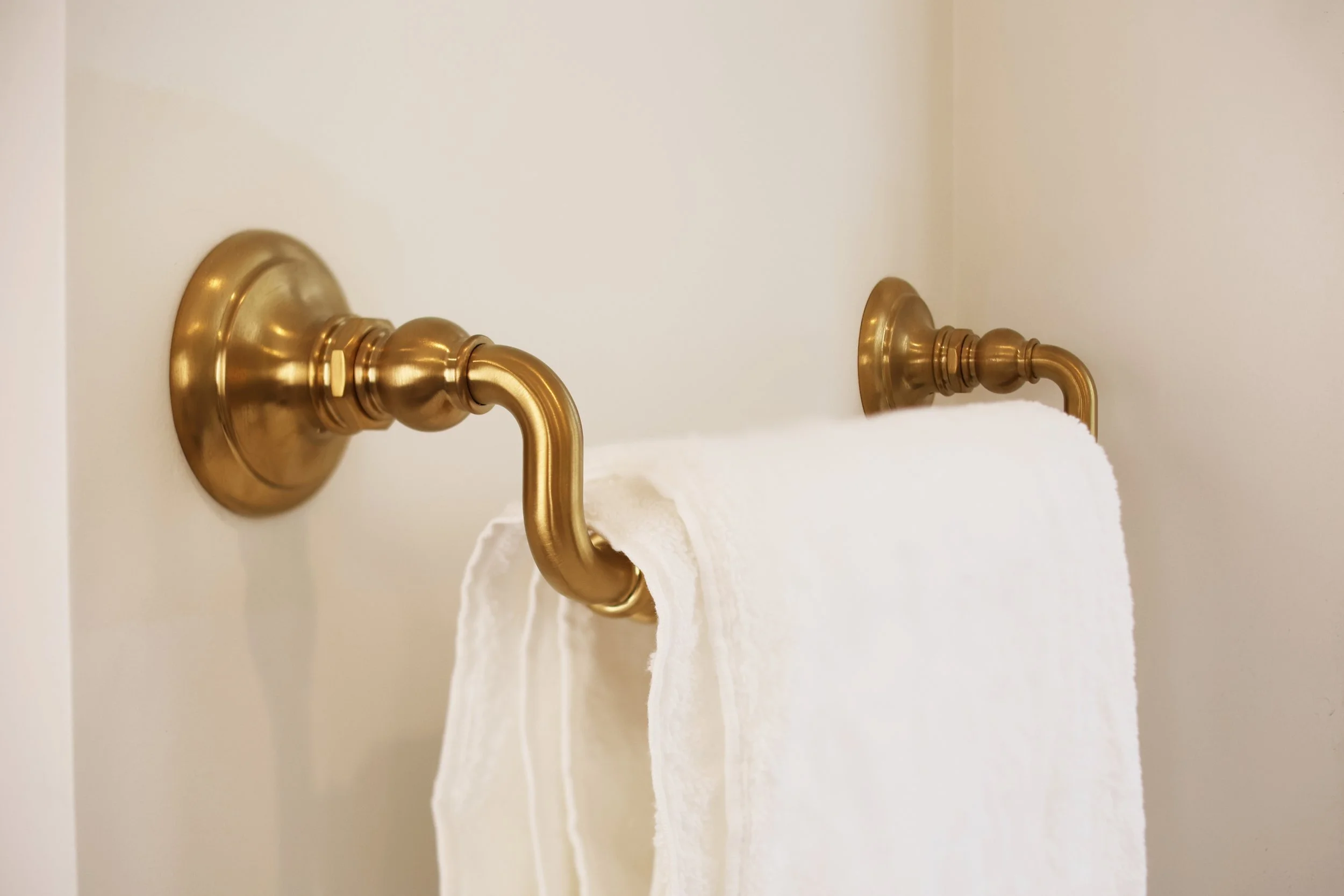 Brass towel bar mounted on a white wall in a black and brass bathroom renovation.