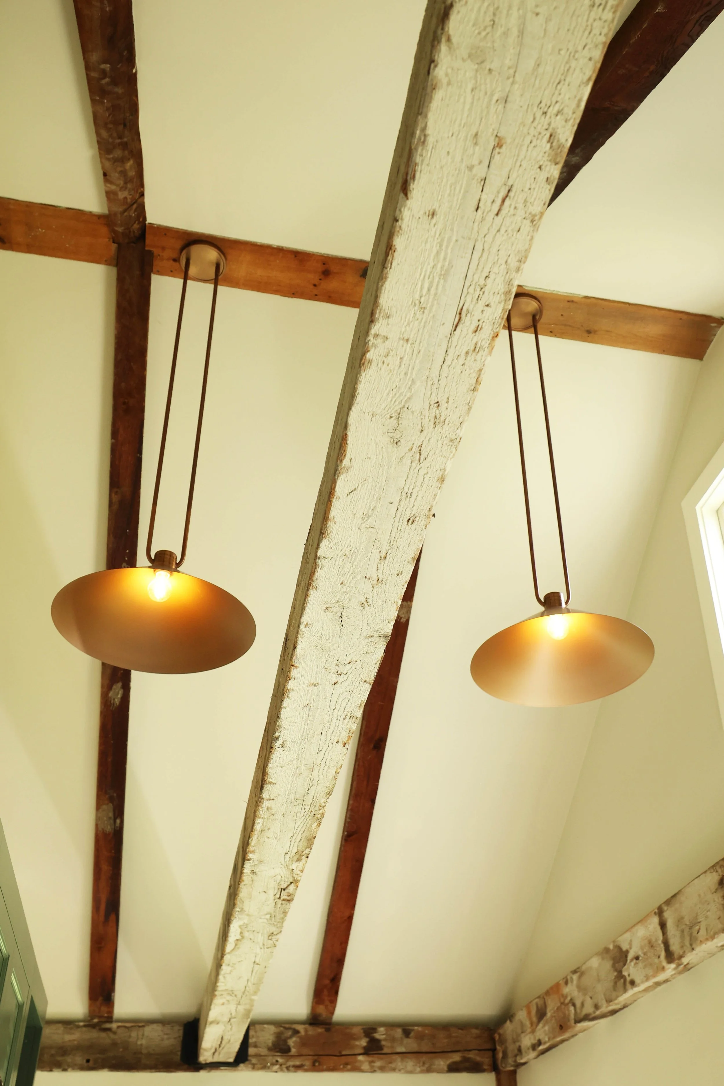 Pendant lights suspended from historic wood beams in a farmhouse mudroom in the Upper Valley.
