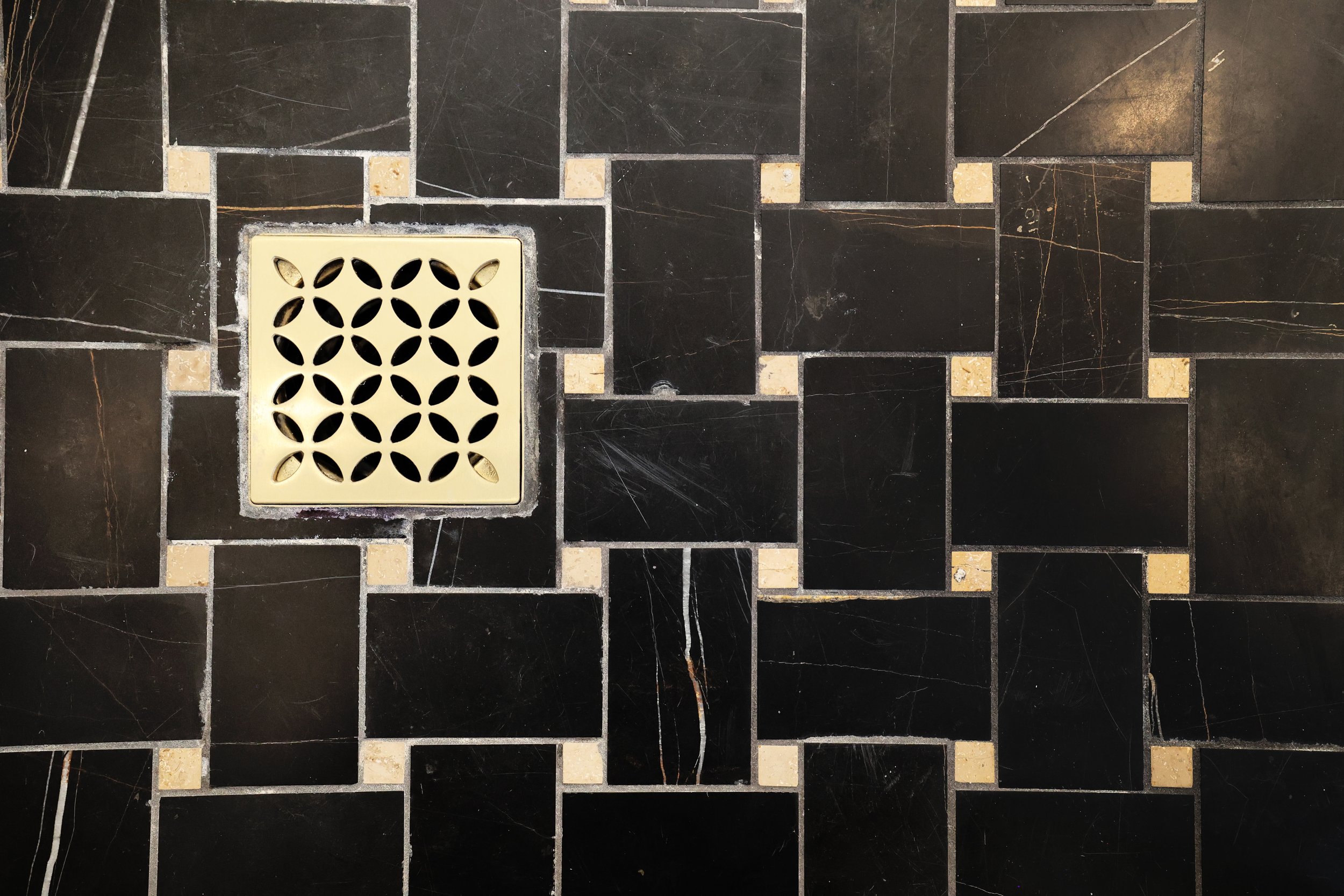 Black shower floor tile with brass drain detail in a Victorian bathroom renovation.