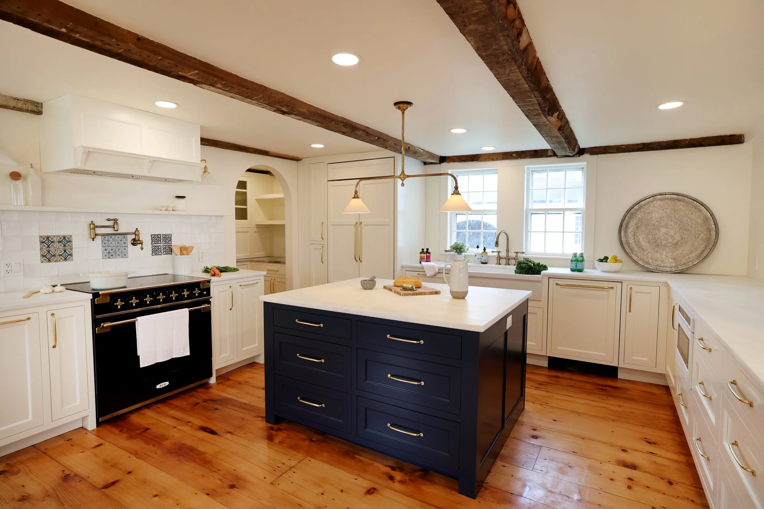 Vermont kitchen renovation featuring a navy island, cream shaker cabinets, marble countertops, and exposed wood beams.