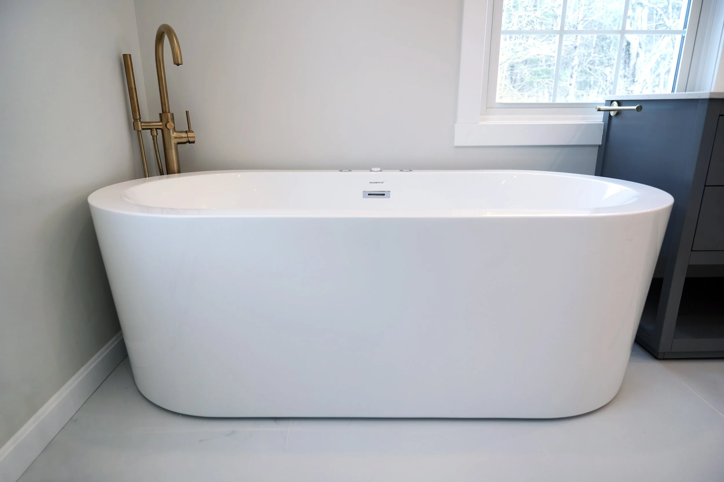 Freestanding modern whirlpool soaking tub with brass floor-mounted filler in an Upper Valley bathroom renovation.