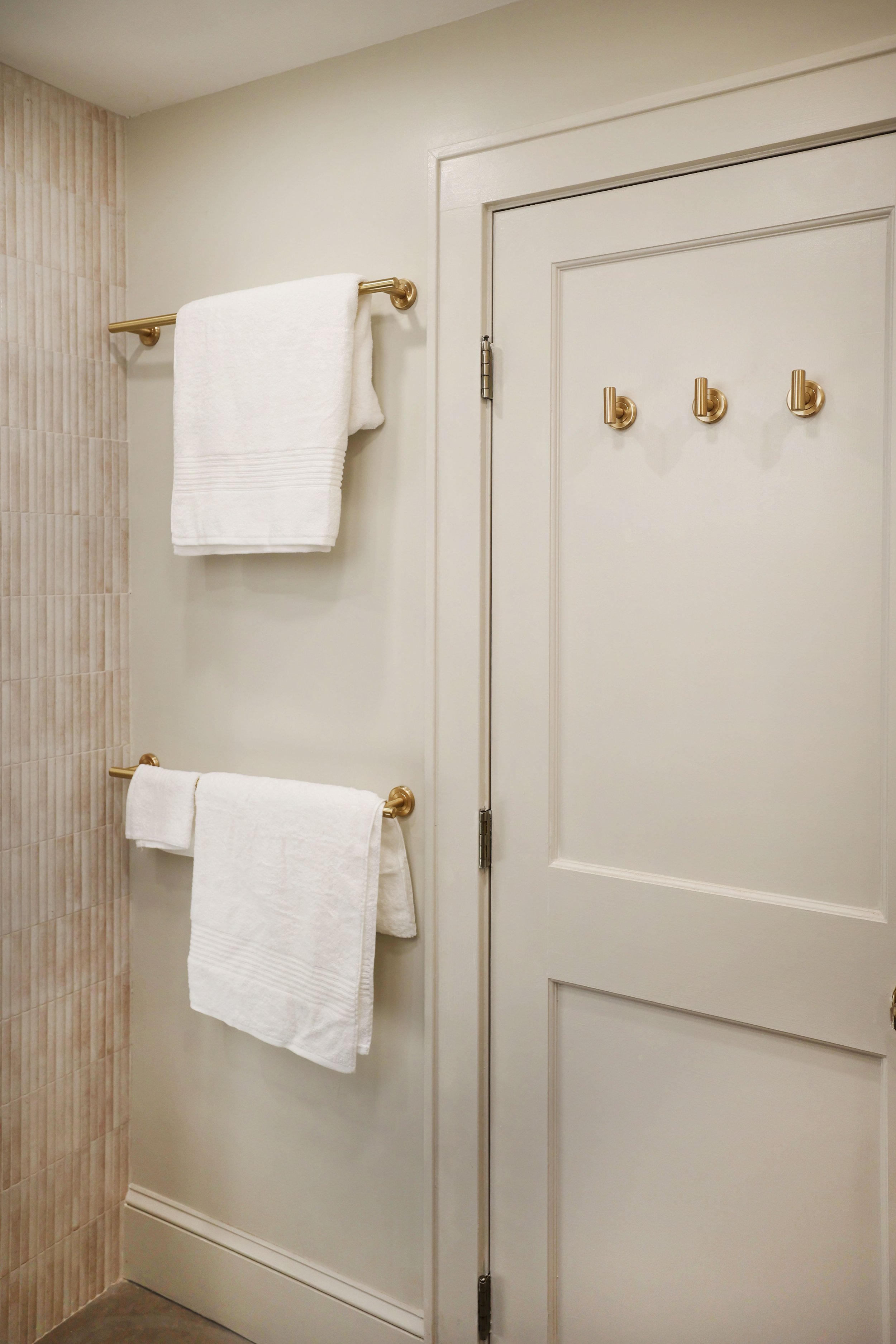 Brass towel bars and wall hooks against soft neutral walls in an organic modern primary bath.