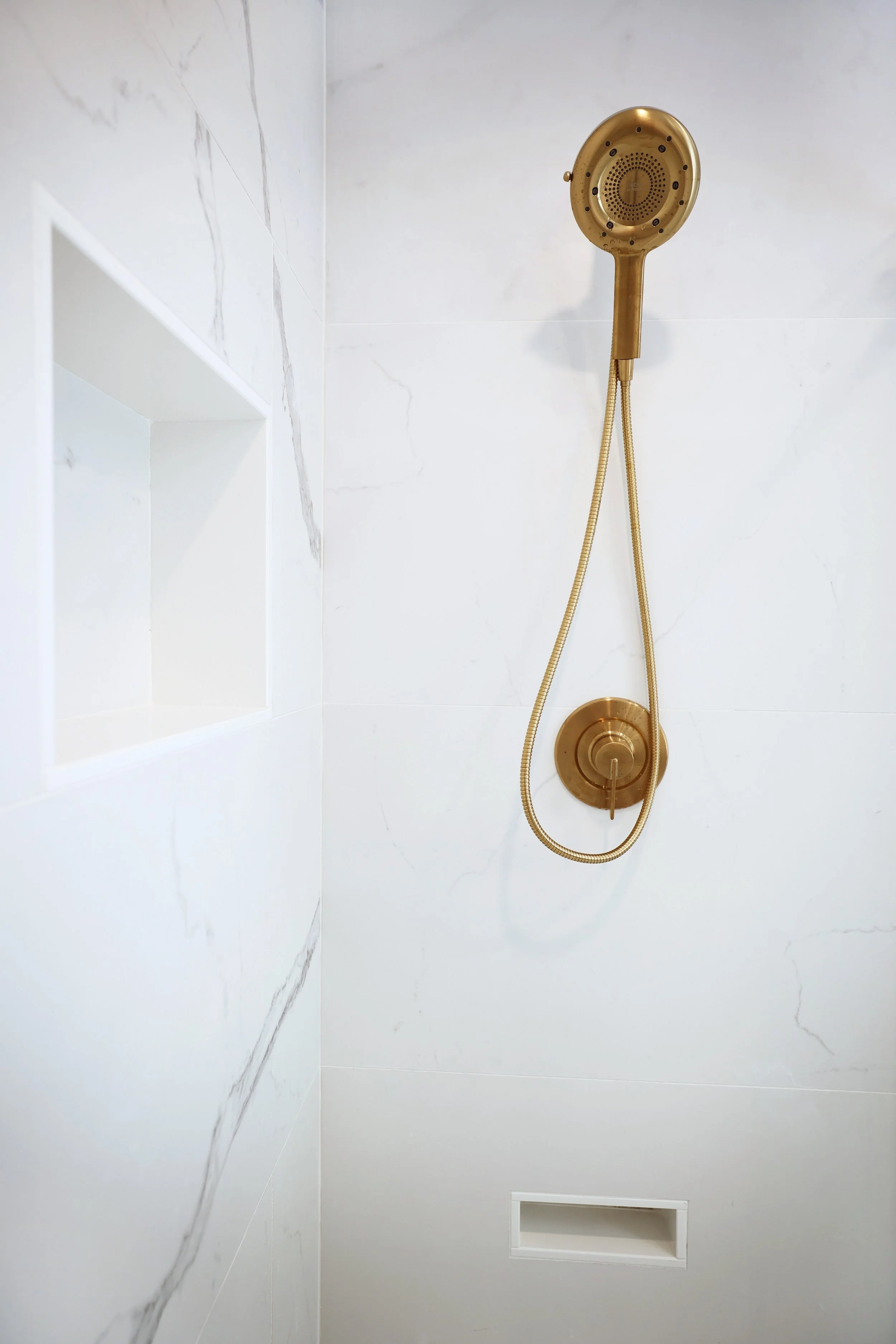 Brass Moen Cia shower fixture mounted on marble-look tile wall.