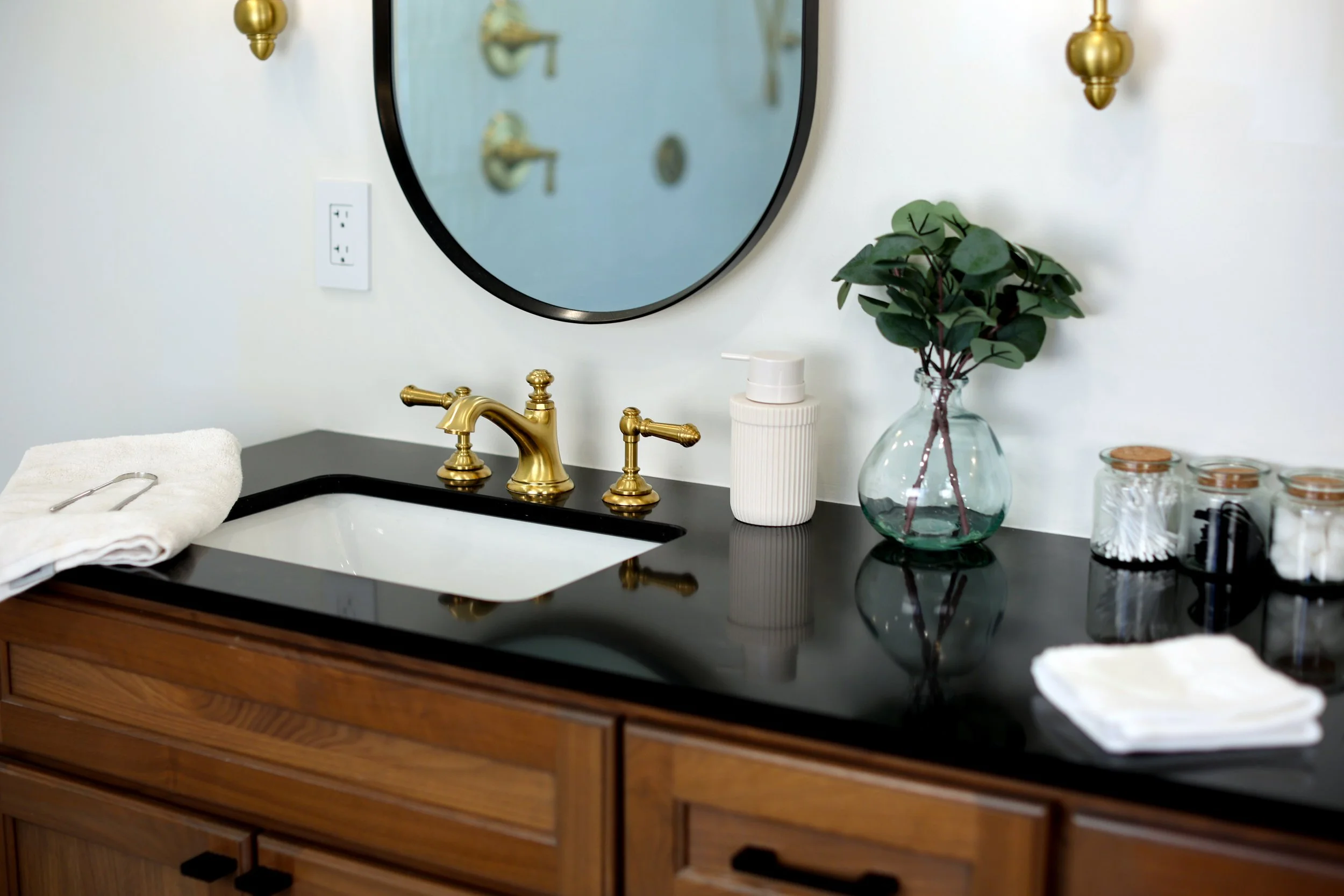 Double vanity with black countertop, brass fixtures, and oval mirrors in a Bethlehem NH Victorian bathroom.