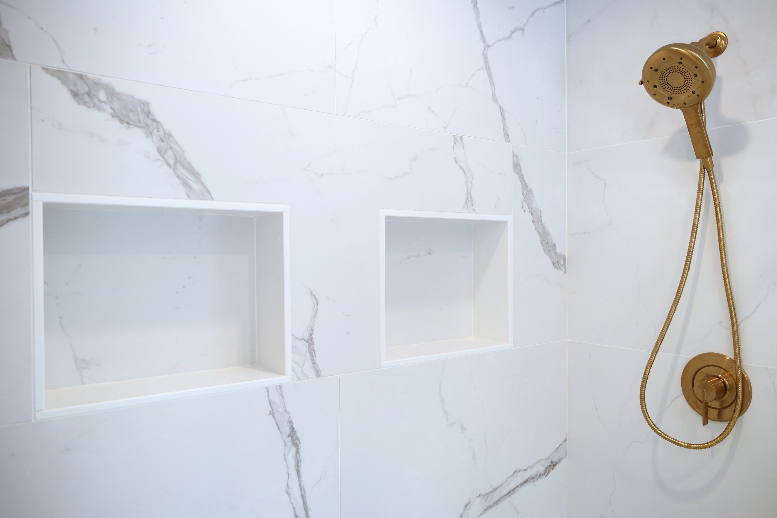 Double recessed shower niches built into marble-look tile wall in a primary bathroom.