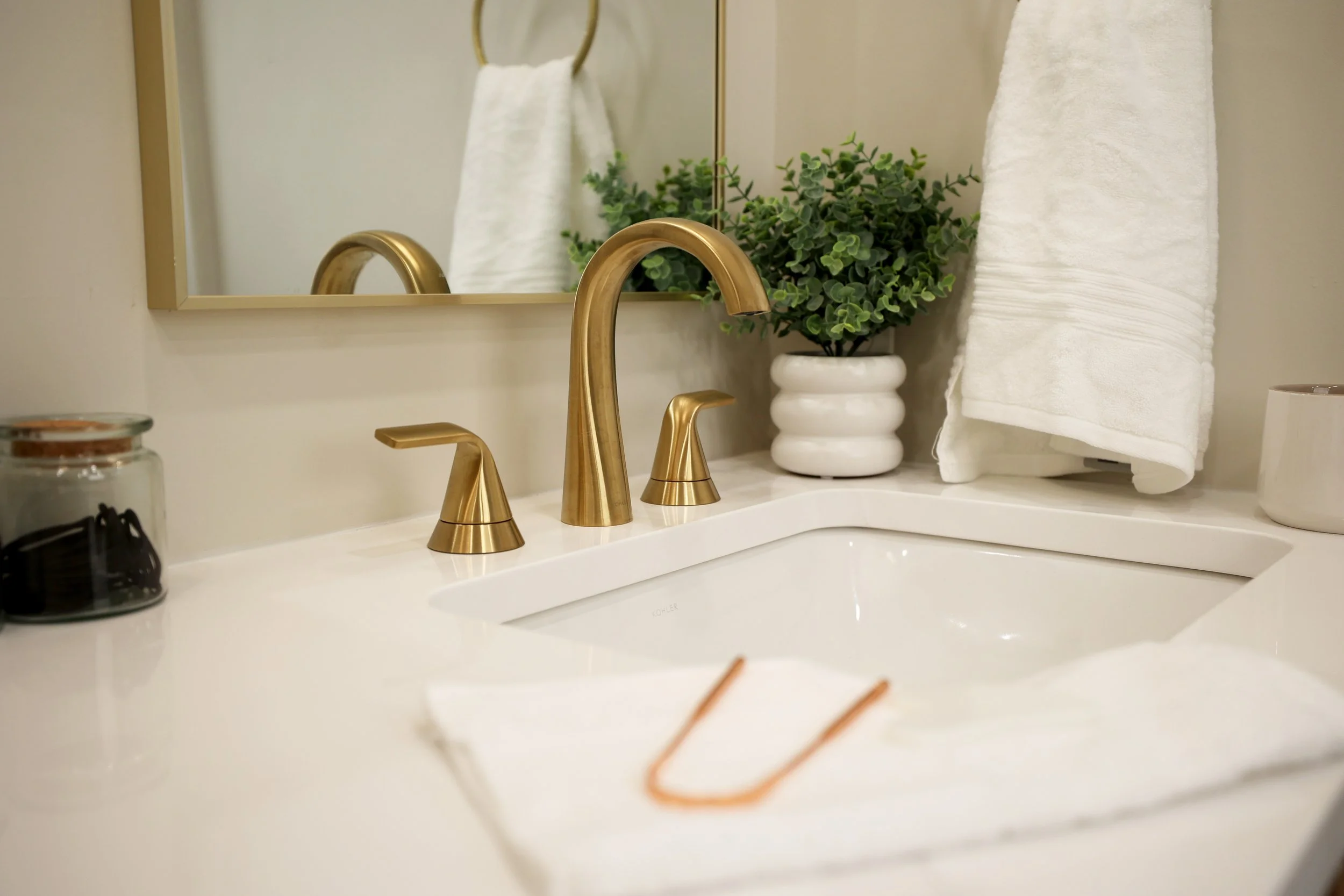 Warm brass faucet over white sink with oak vanity and soft neutral finishes in organic modern primary bath.