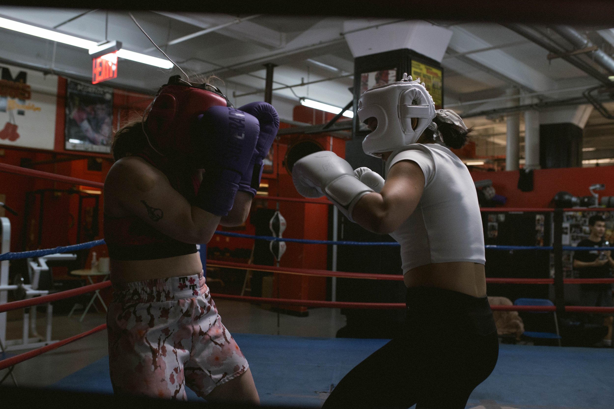 Two female boxers sparring in a ring, wearing protective headgear and gloves.