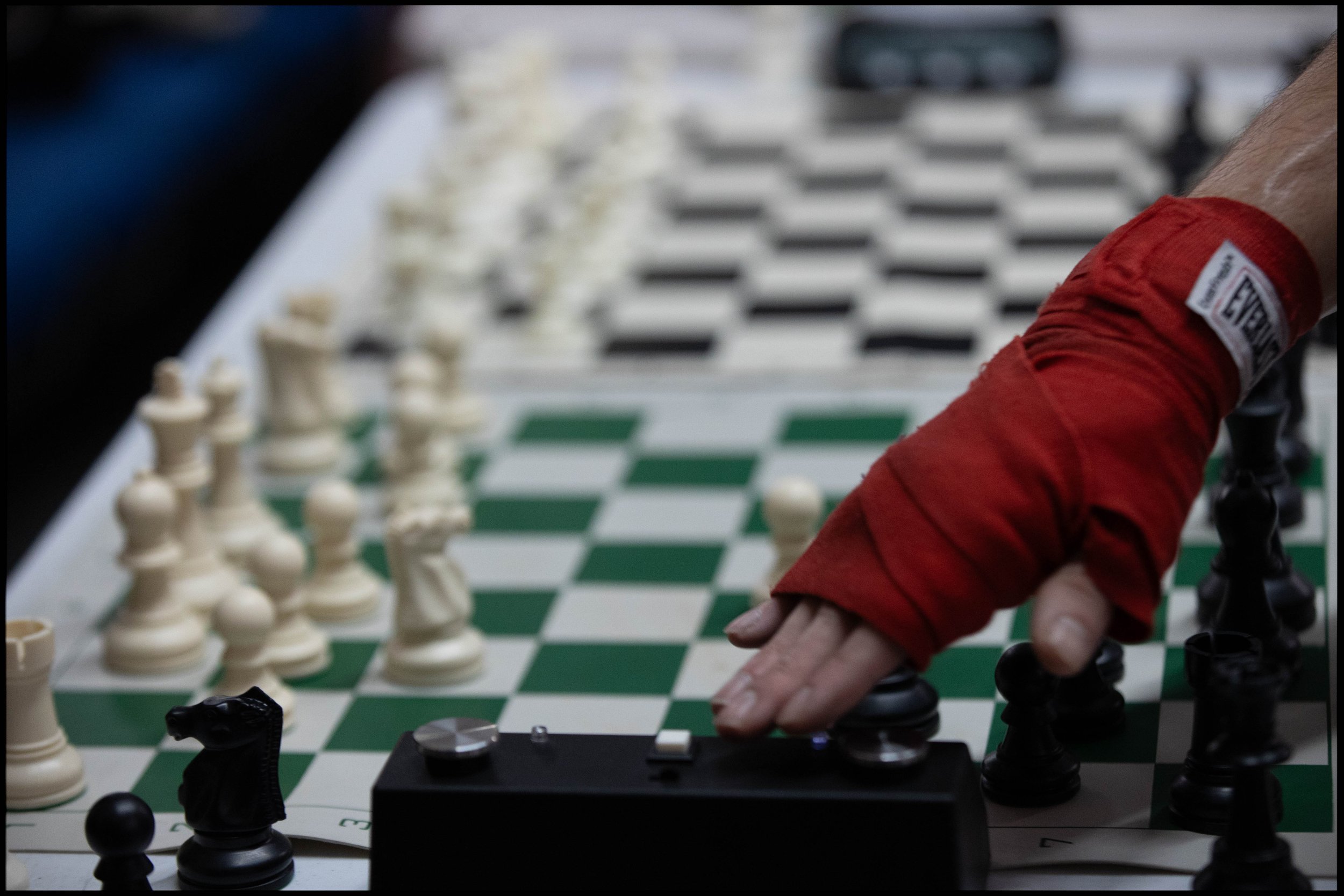 Chess board with a person's hand in a red wrap pressing a chess clock button, pieces mid-game.