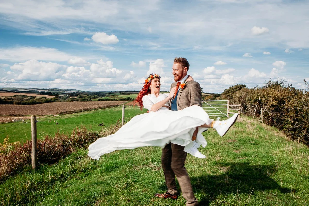 Fun, candid wedding moment of bride being lifted and laughing in the countryside, natural wedding photography Isle of Wight