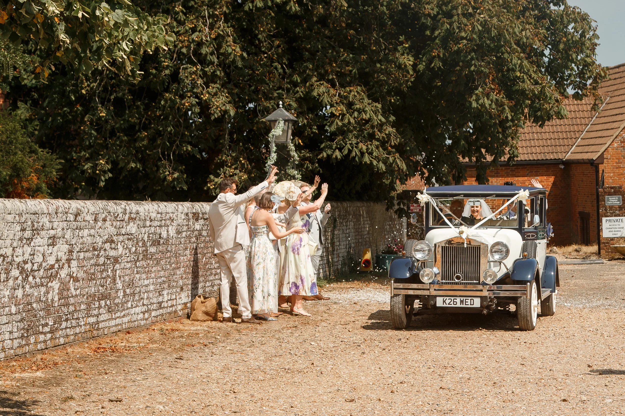 Newlyweds leaving their wedding ceremony in a vintage car as guests wave them off