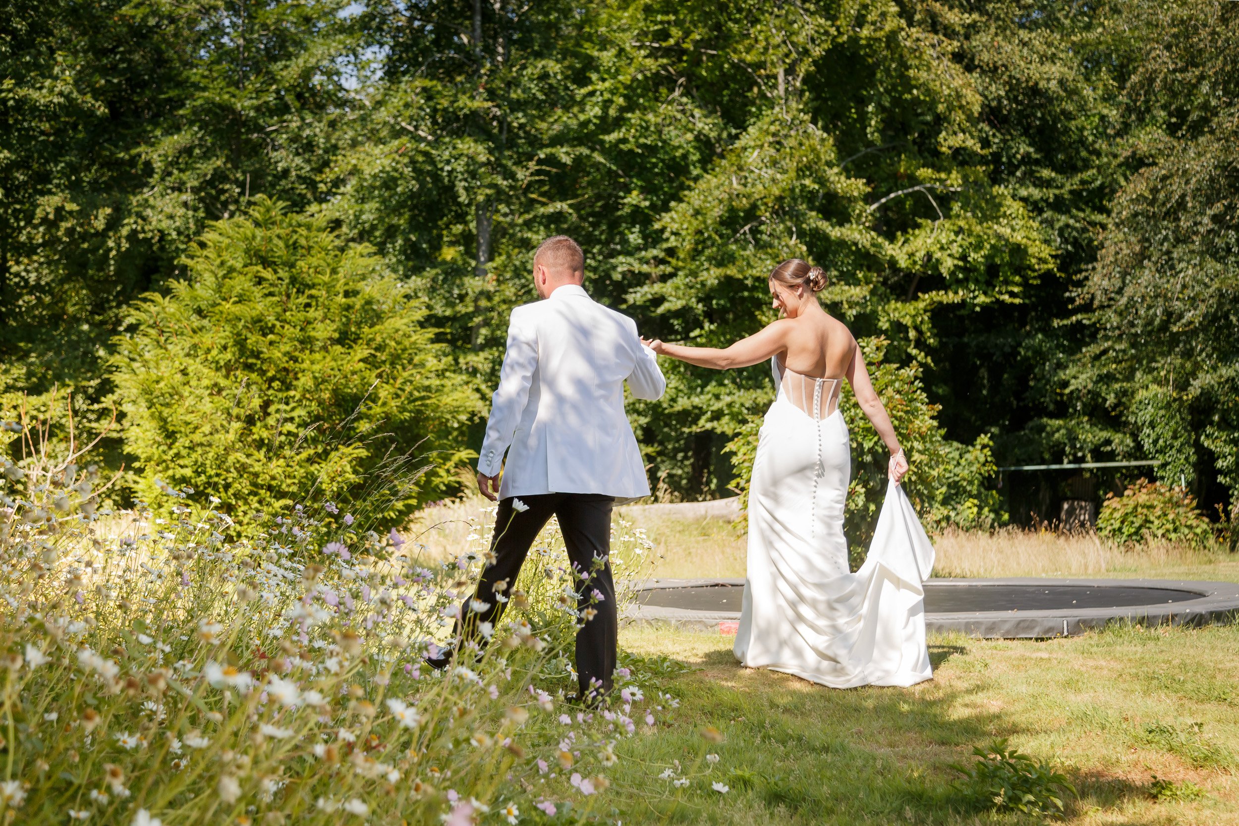 Bride and groom walking hand in hand through a sunny garden on their wedding day