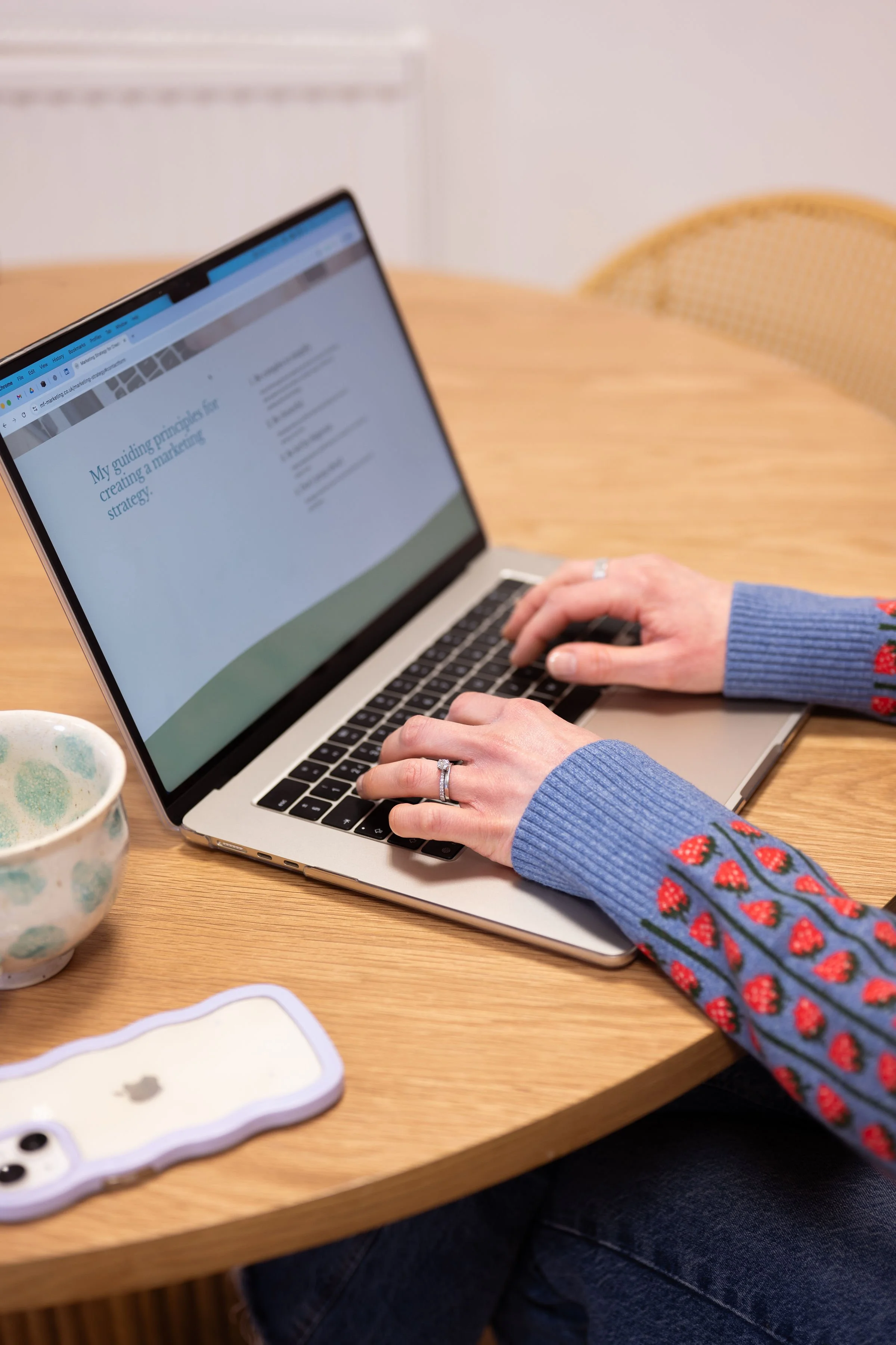 Hands typing at laptop, with mug and phone on table