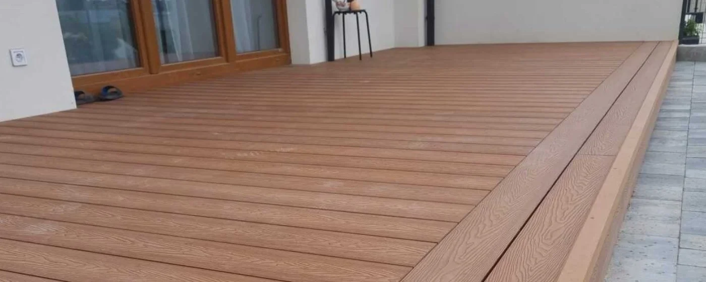 A wooden deck outside a house with sliding glass doors, a couple of shoes, and a chair in the background.