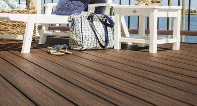 Close-up of a wooden deck with a white bench, a patterned bag, and a pair of flip-flops.