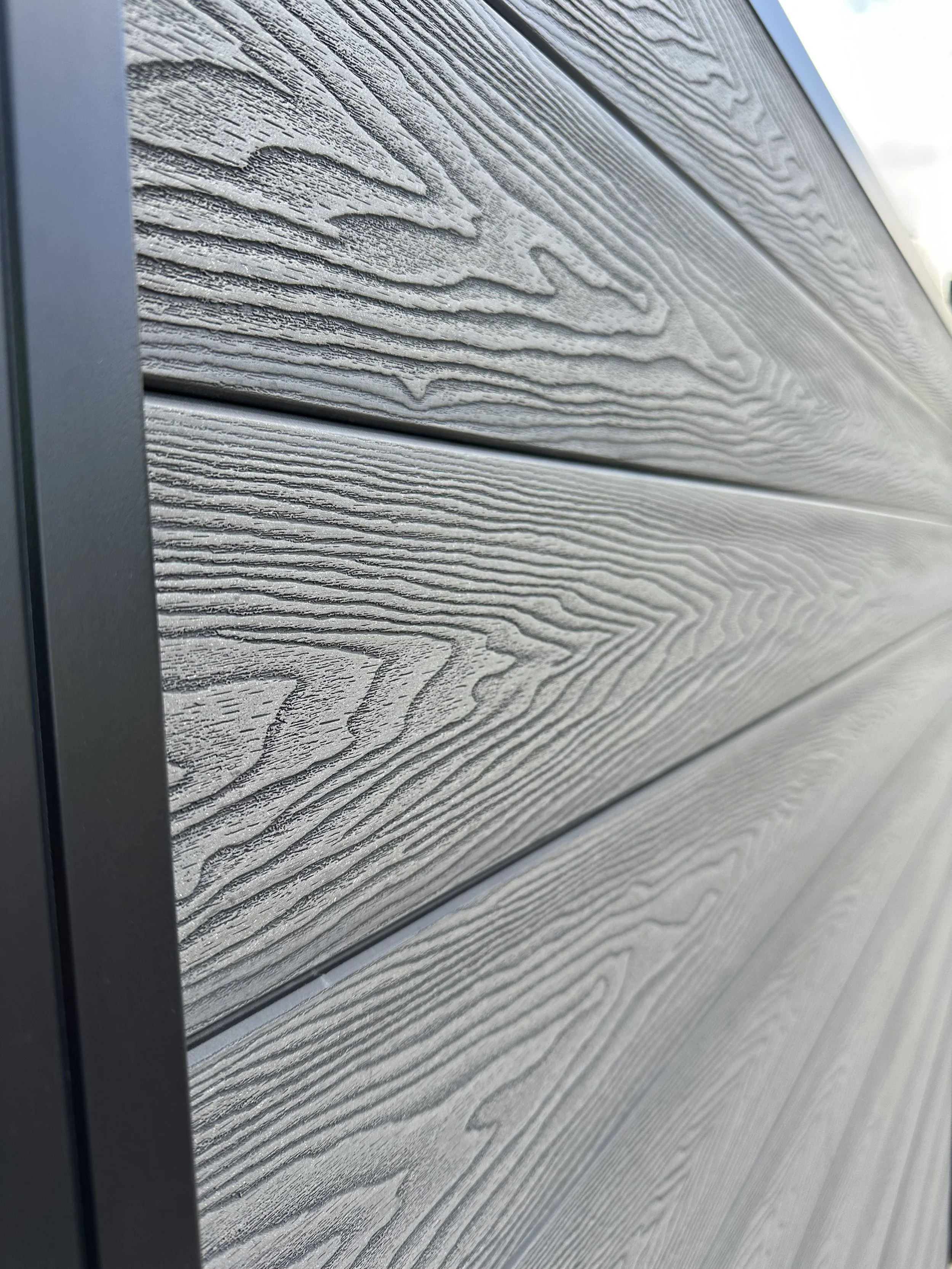 Close-up of a wall with horizontal wooden panels in gray-gray color with detailed wood grain patterns, bordered on the left by a dark gray vertical trim.