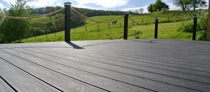 View of a wooden deck overlooking a green field with a horse in the distance, fencing, and trees.