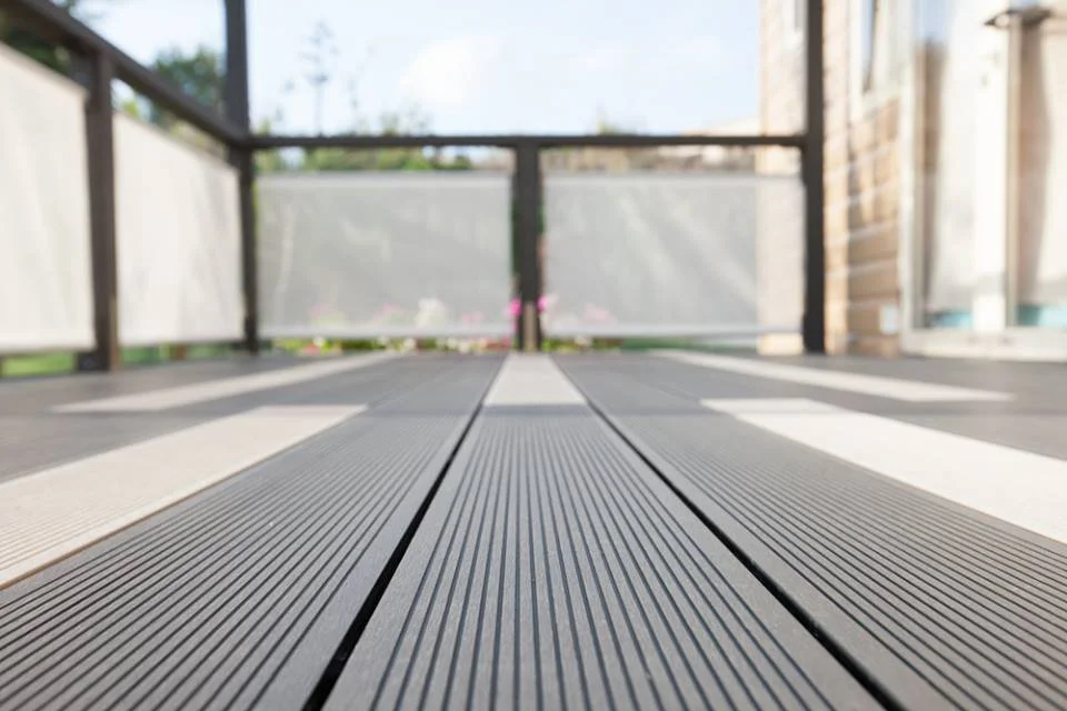 Low angle view of a balcony deck with wooden planks, railing, and a blurry background of trees and sky.
