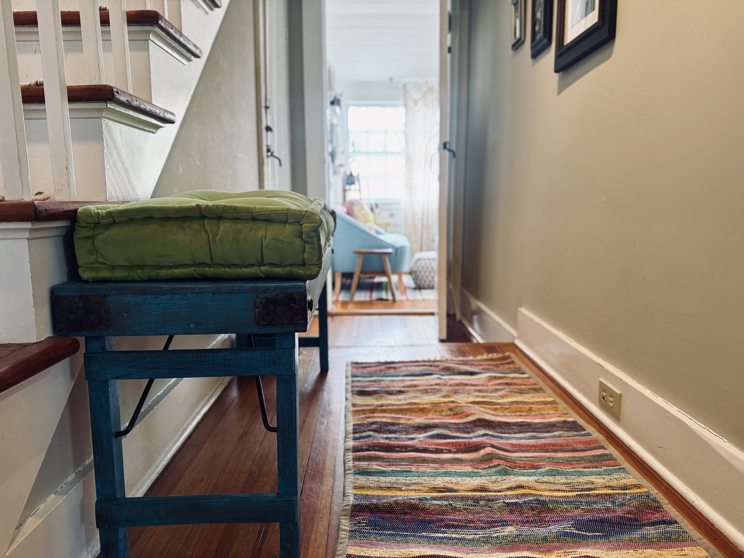 Home hallway with green cushion on blue wooden bench, multicolored striped rug, and staircase
