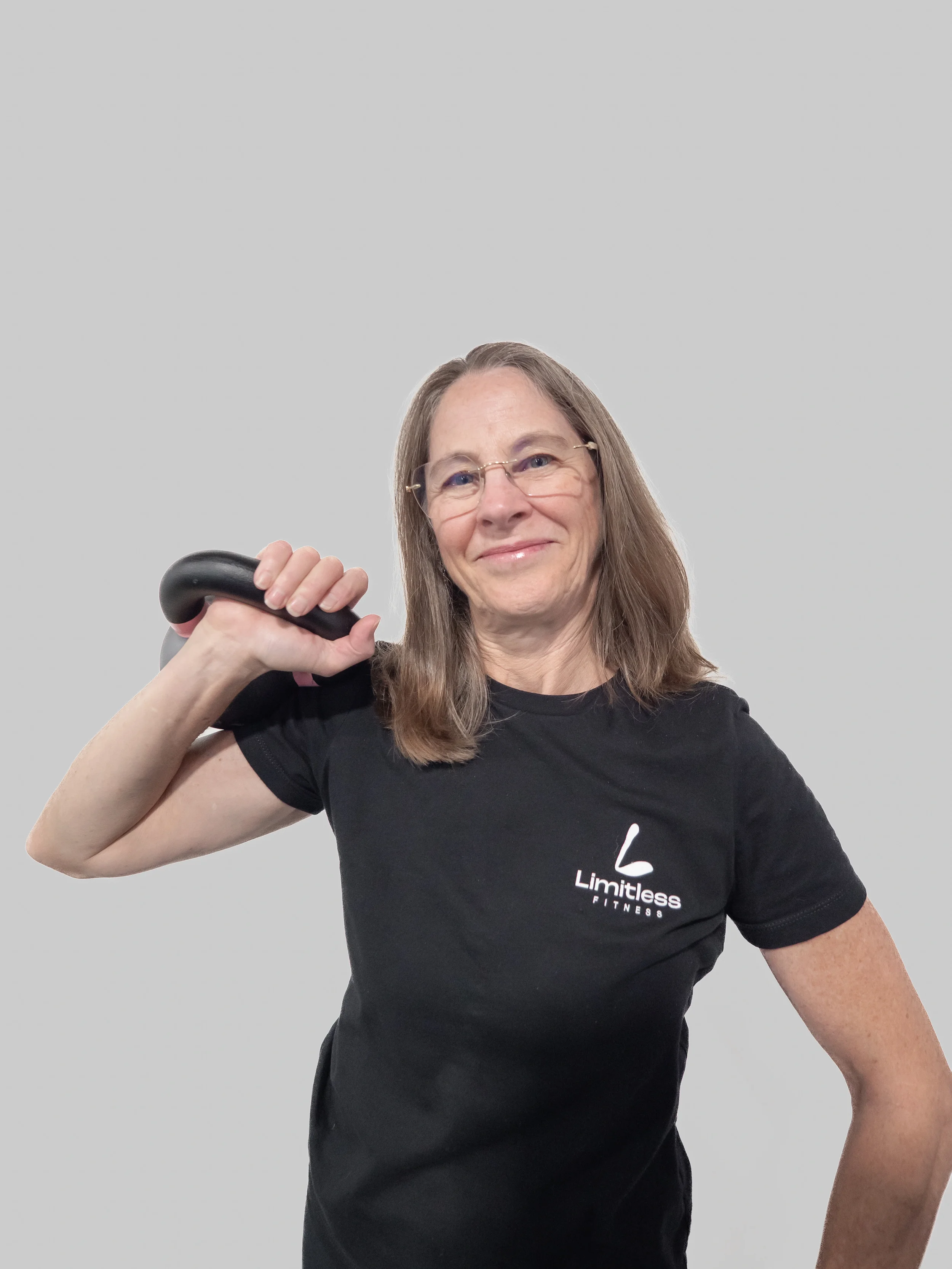 Woman on a golf course wearing sunglasses, a light gray shirt, and blue shorts, holding a golf club and giving a thumbs-up gesture with her right hand, with palm trees and mountains in the background.