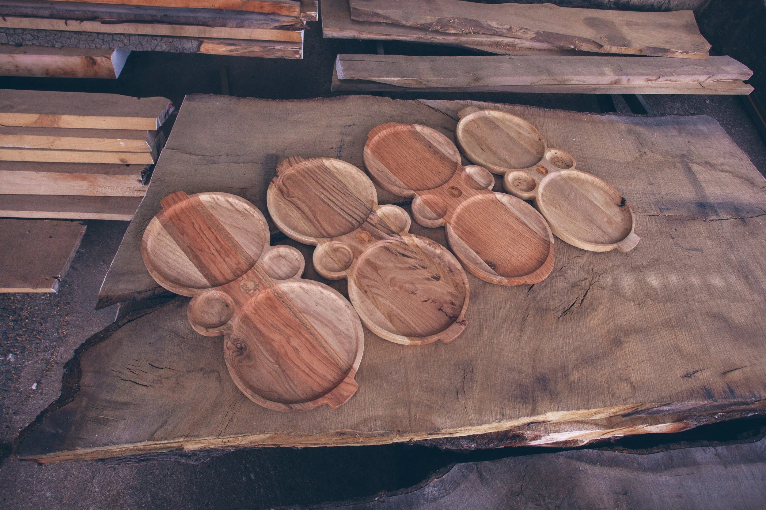 Various unfinished wooden plates and bowls on a rustic wooden table in a woodworking shop.