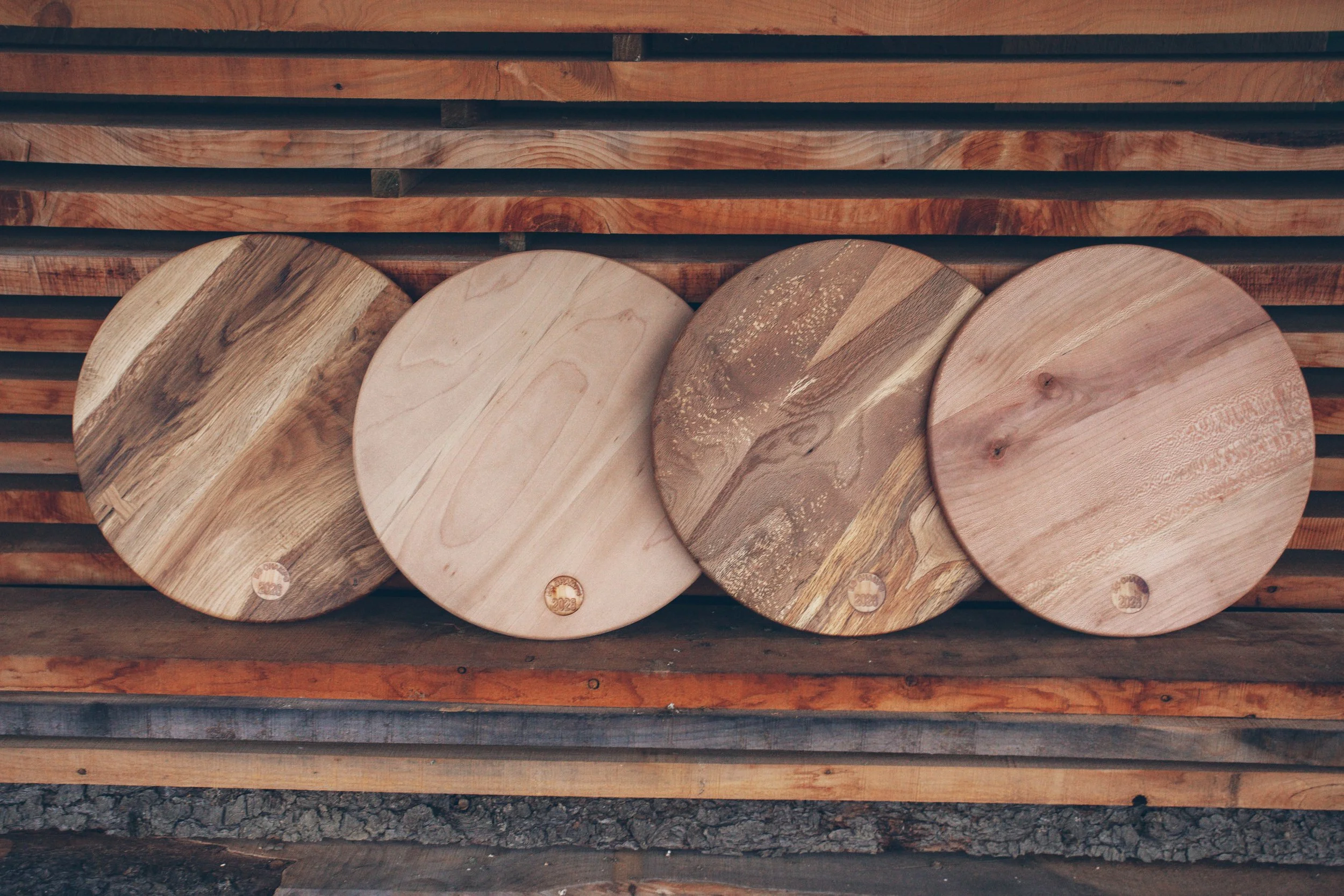 Four wooden round cutting boards leaning against a wooden slat wall.