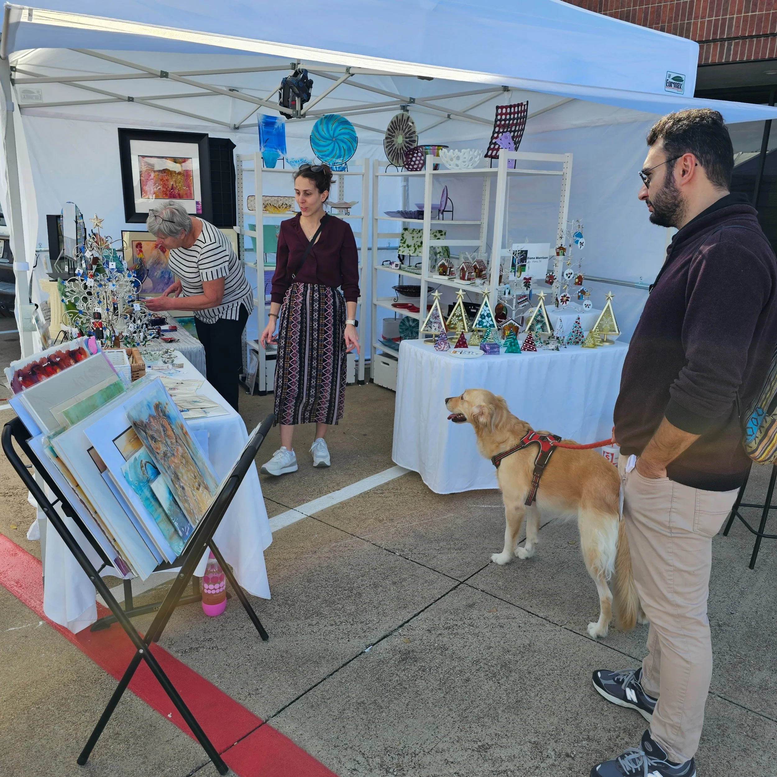 People shopping at The craft Guild art show and sale two ladies and a man with a dog