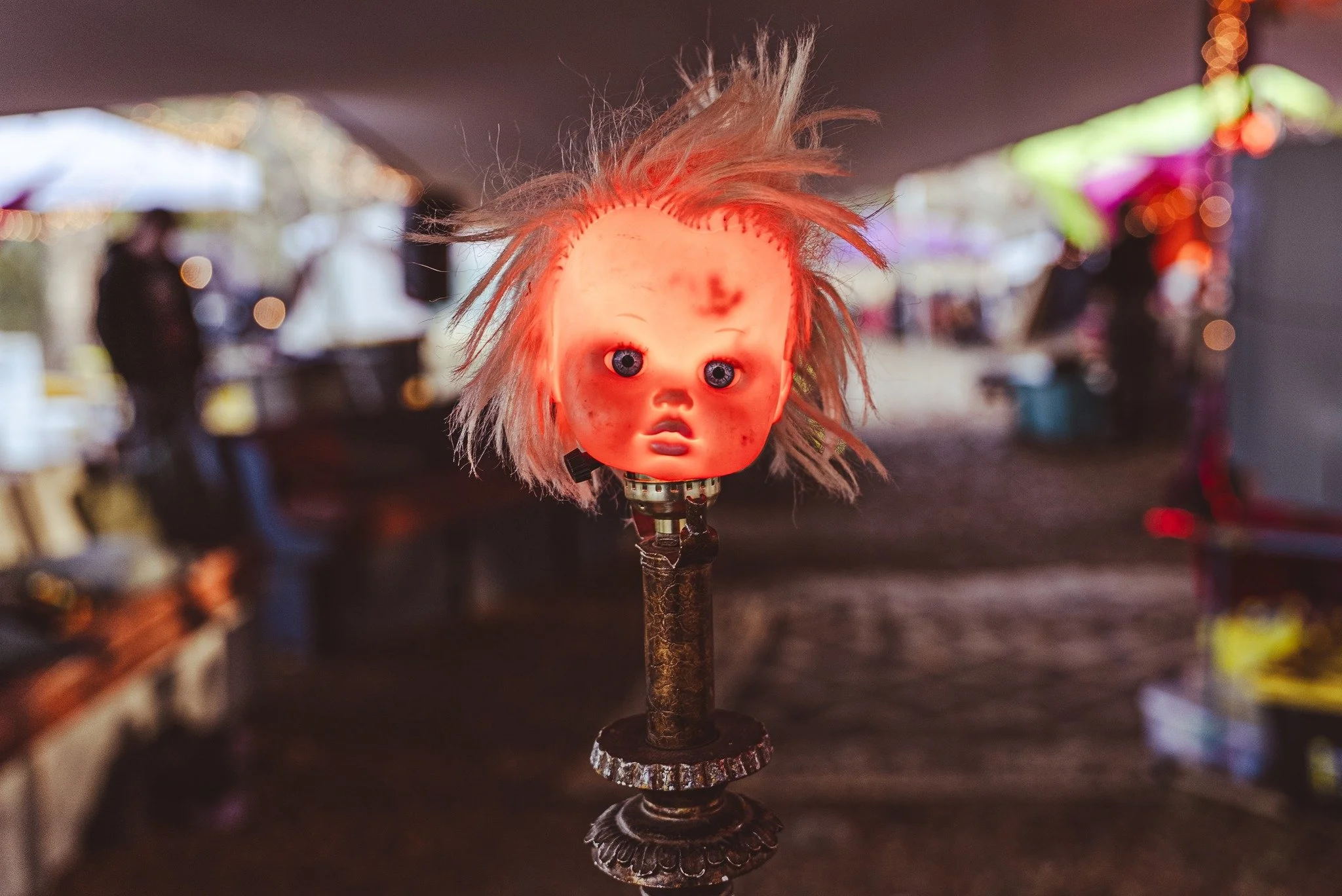 A creepy, doll head with wild, unkempt hair and a distressed face, mounted on a rusted metal stand.