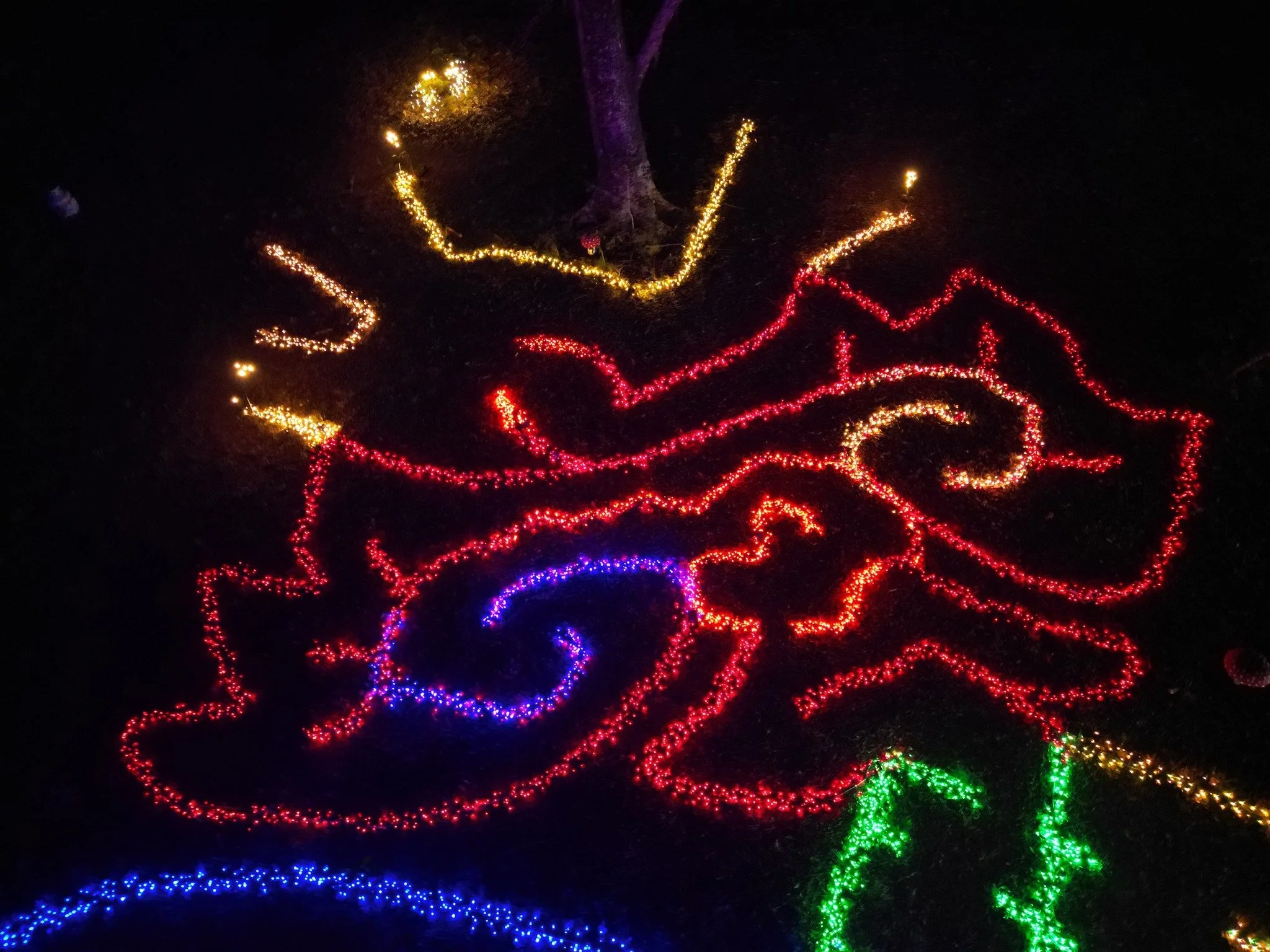 Colorful Christmas lights arranged in the shape of a large Santa Claus face with a hat and beard, illuminated on a dark background.