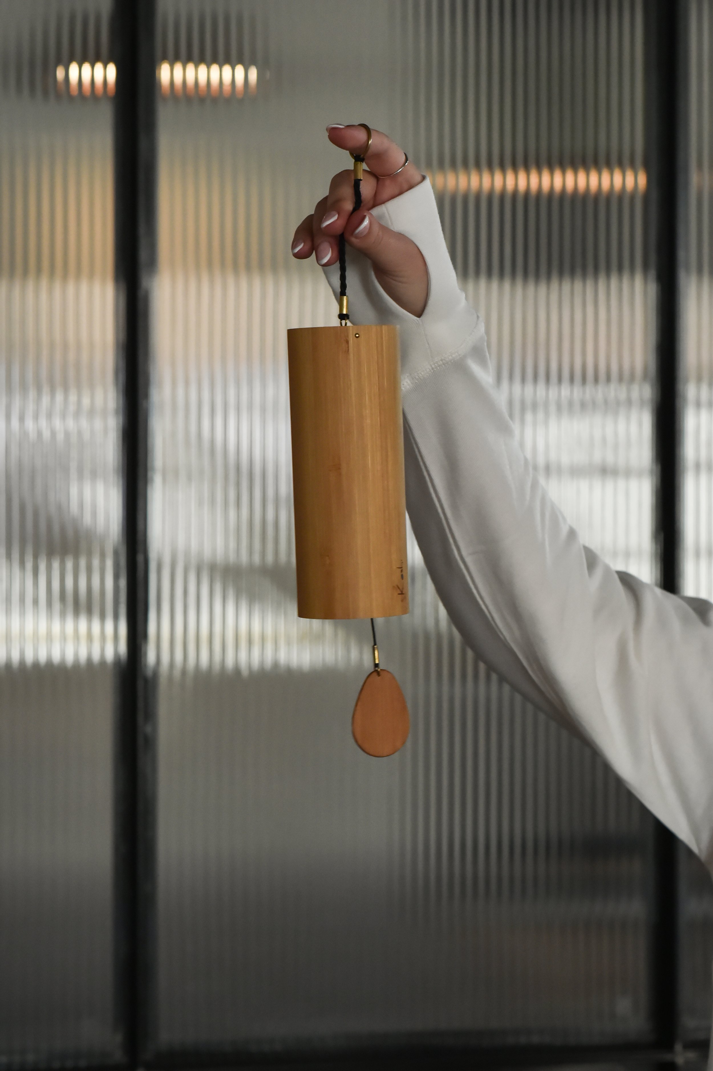 A person's hand holding a bamboo wind chime indoors.