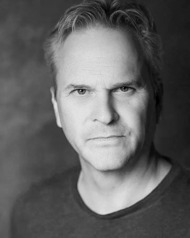 Jeremy Todd, personal bio acting photo headshot. Black and white close-up portrait of a middle-aged man with short, wavy hair, looking directly at the camera with a serious expression, wearing a dark shirt.
