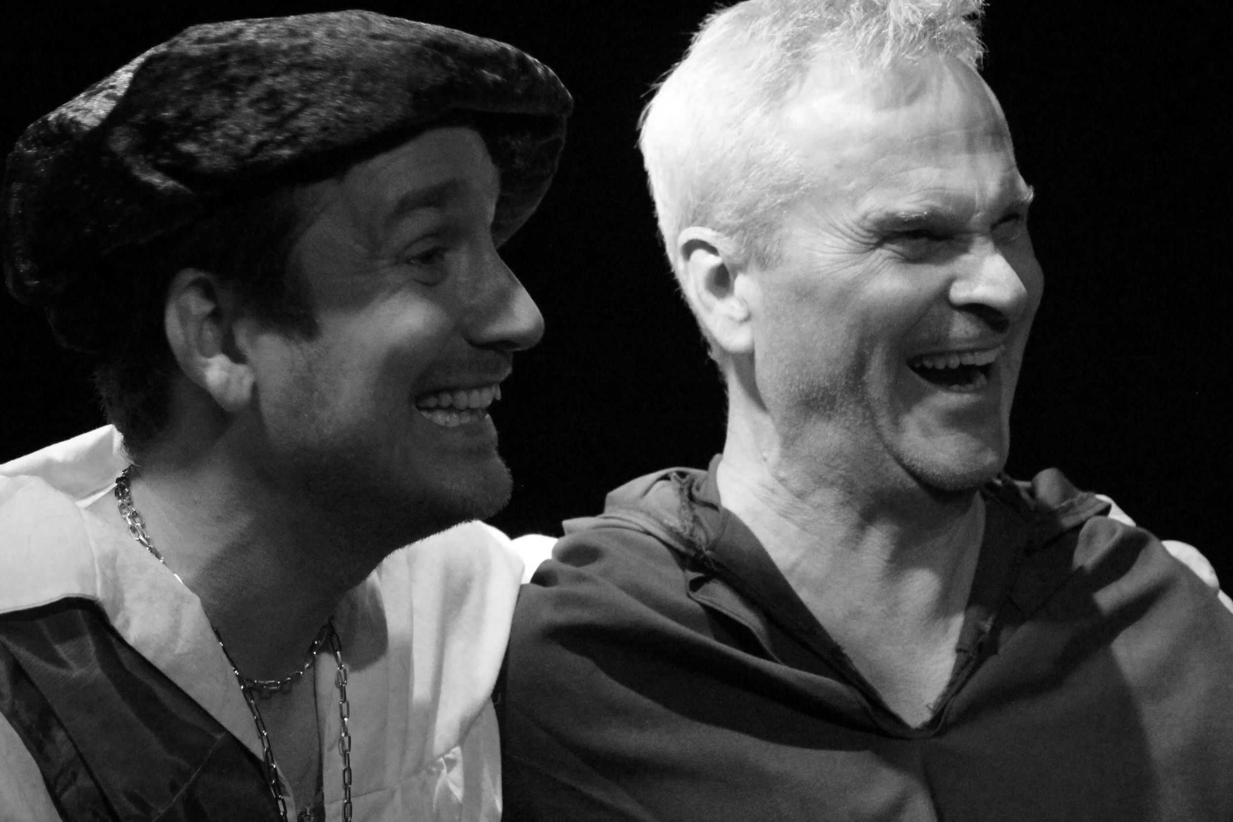 Jeremy todd acting photo. Two men are smiling and laughing together; one has a dark hat and chain necklace, the other has short gray hair and is wearing a jacket.