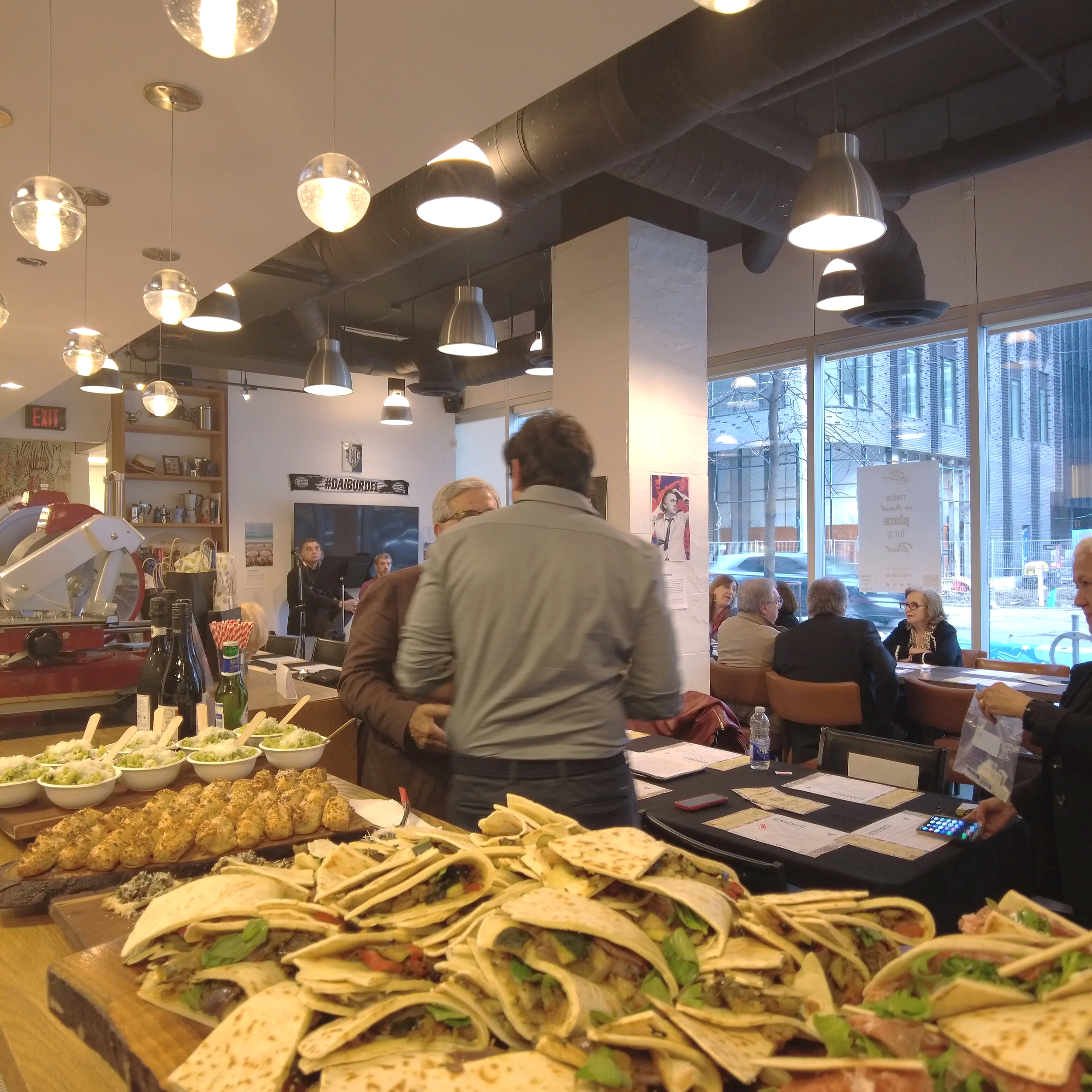 Display of various tacos on wooden platters in a restaurant with industrial ceiling lighting and large windows.