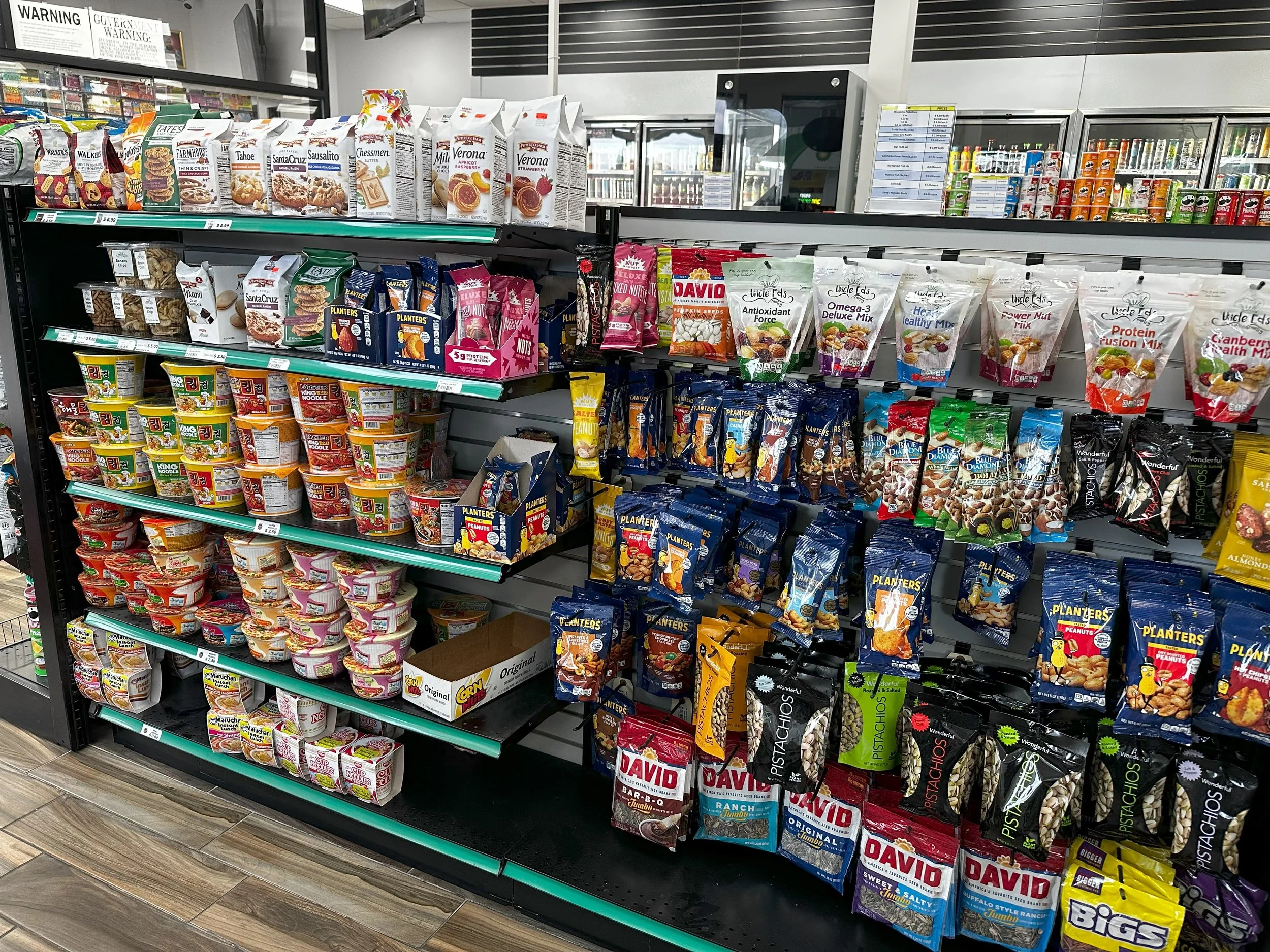 Assorted snack aisle in a convenience store, featuring nuts, seeds, cookies, and instant noodles.