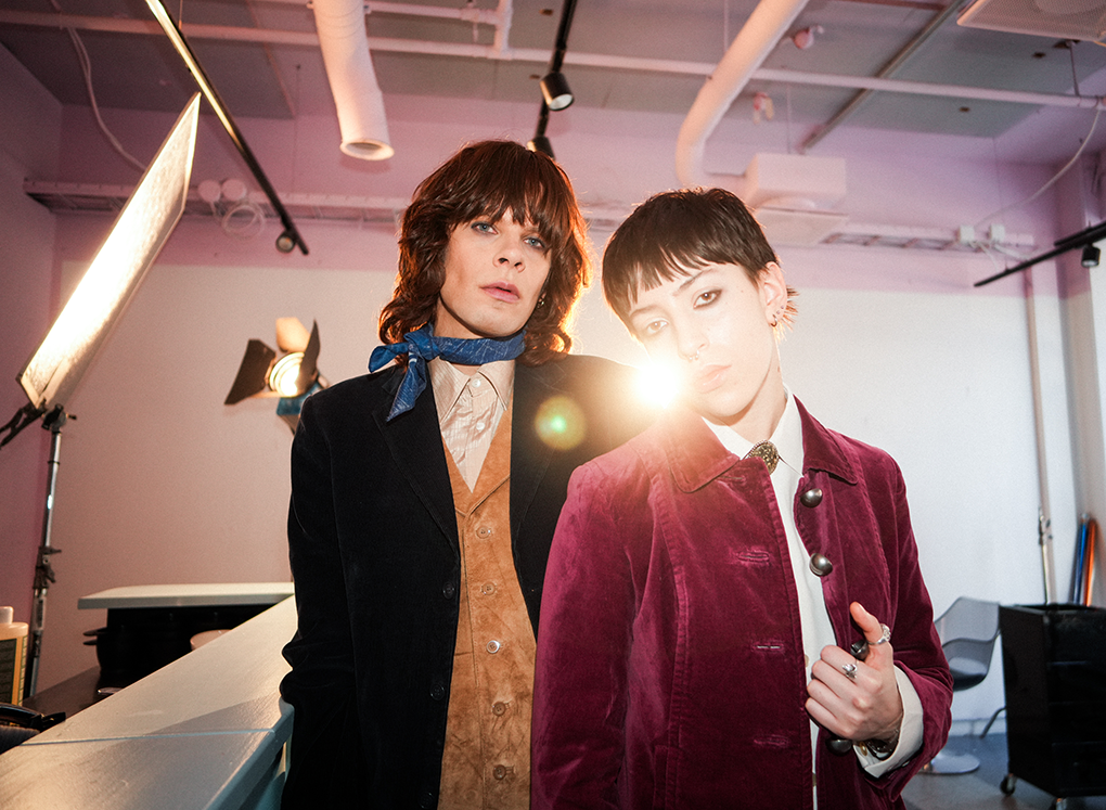 Two young adults posing in a photography studio with studio lights and equipment in the background.