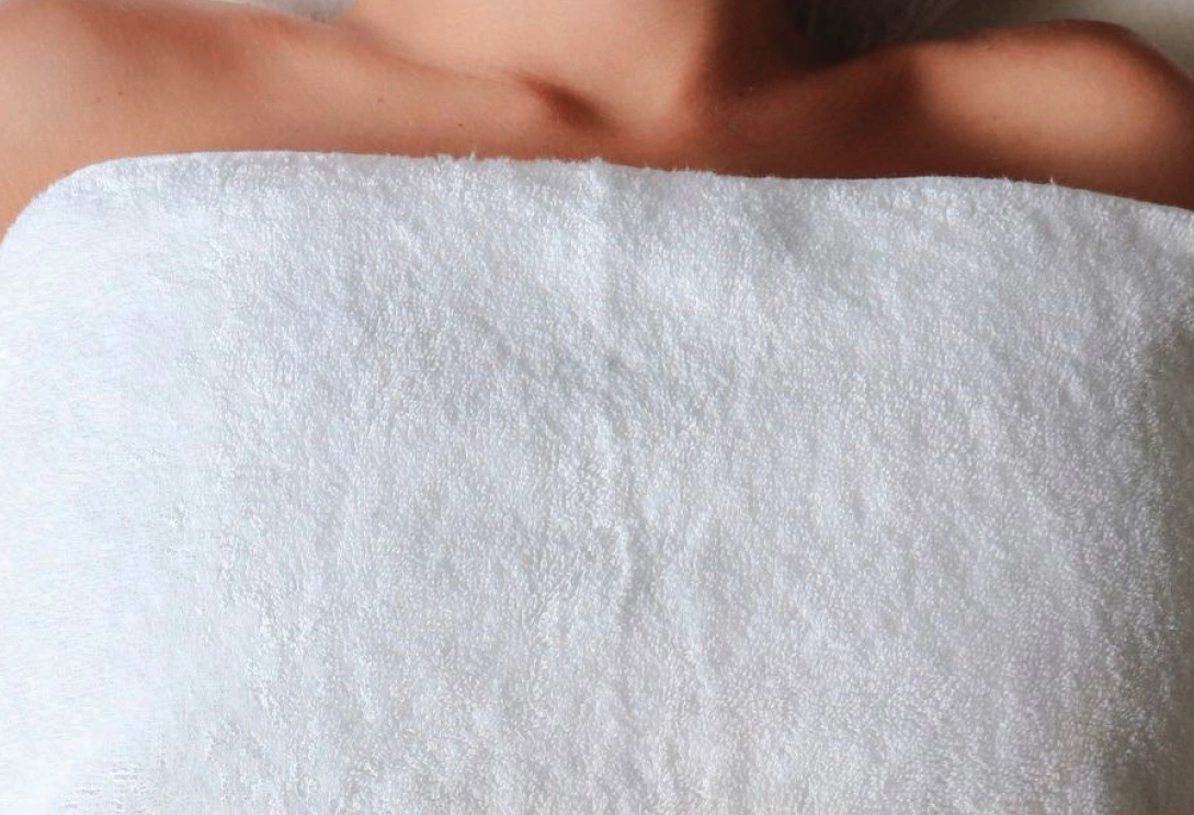 Partially visible person's shoulder and neck above a white towel or blanket.