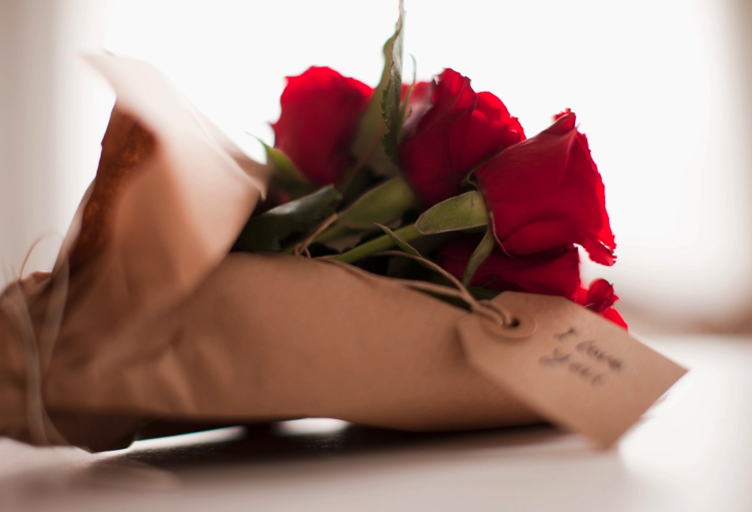 Red roses wrapped in brown paper with a handwritten tag.