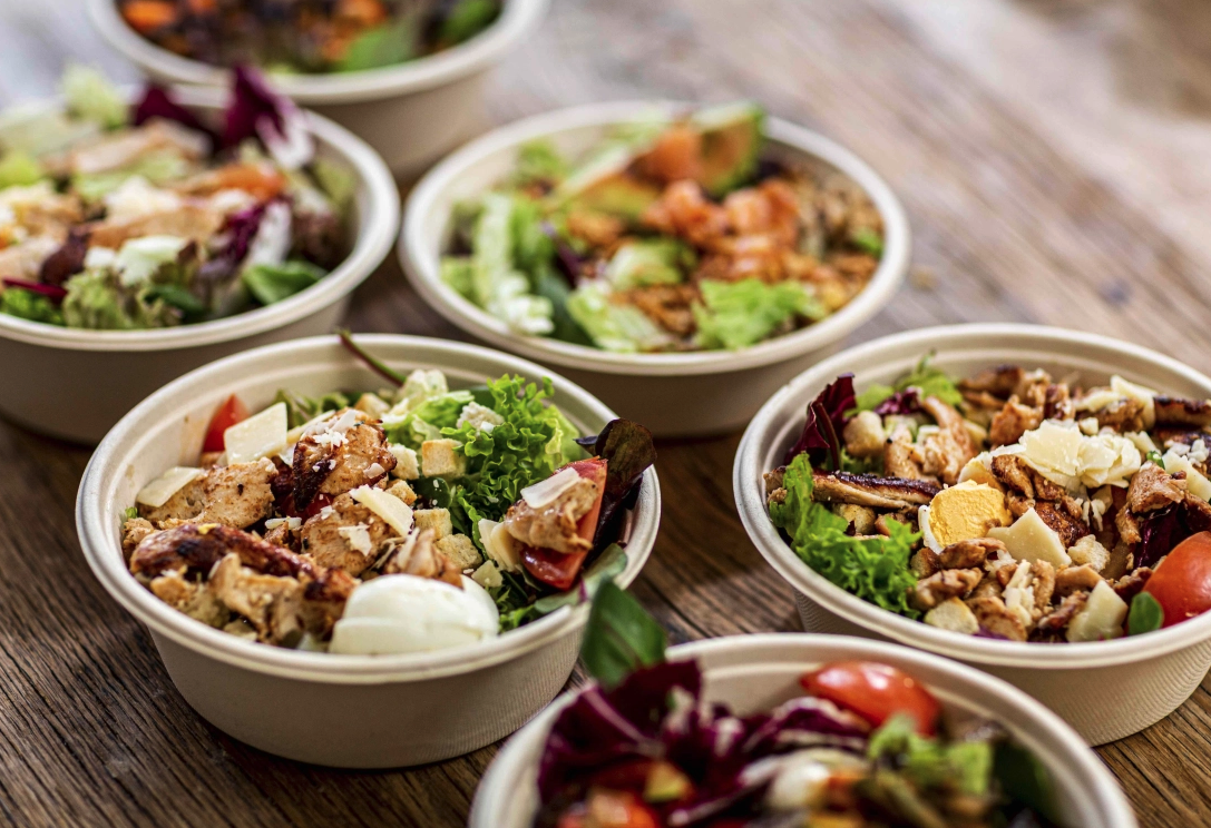 Multiple bowls of salad with lettuce, tomatoes, cheese, and grilled chicken on a wooden table.
