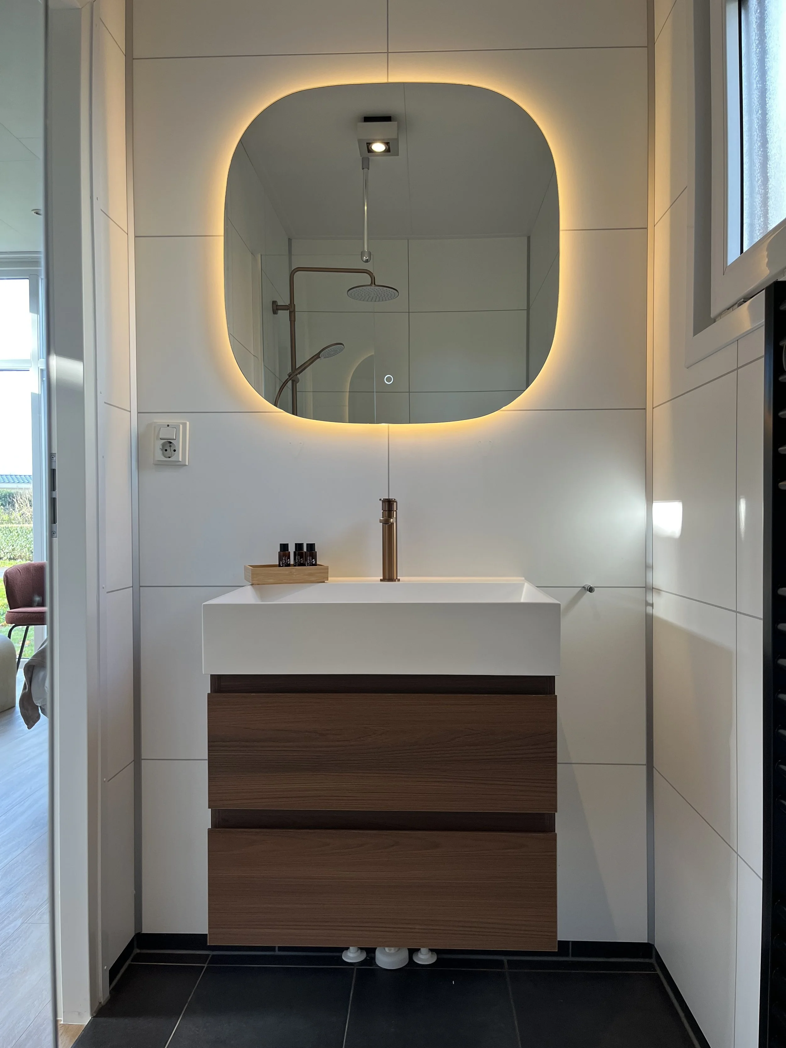 Een eetkamer met een houten tafel, zes houten stoelen en een grote raampartij met uitzicht op een tuin.