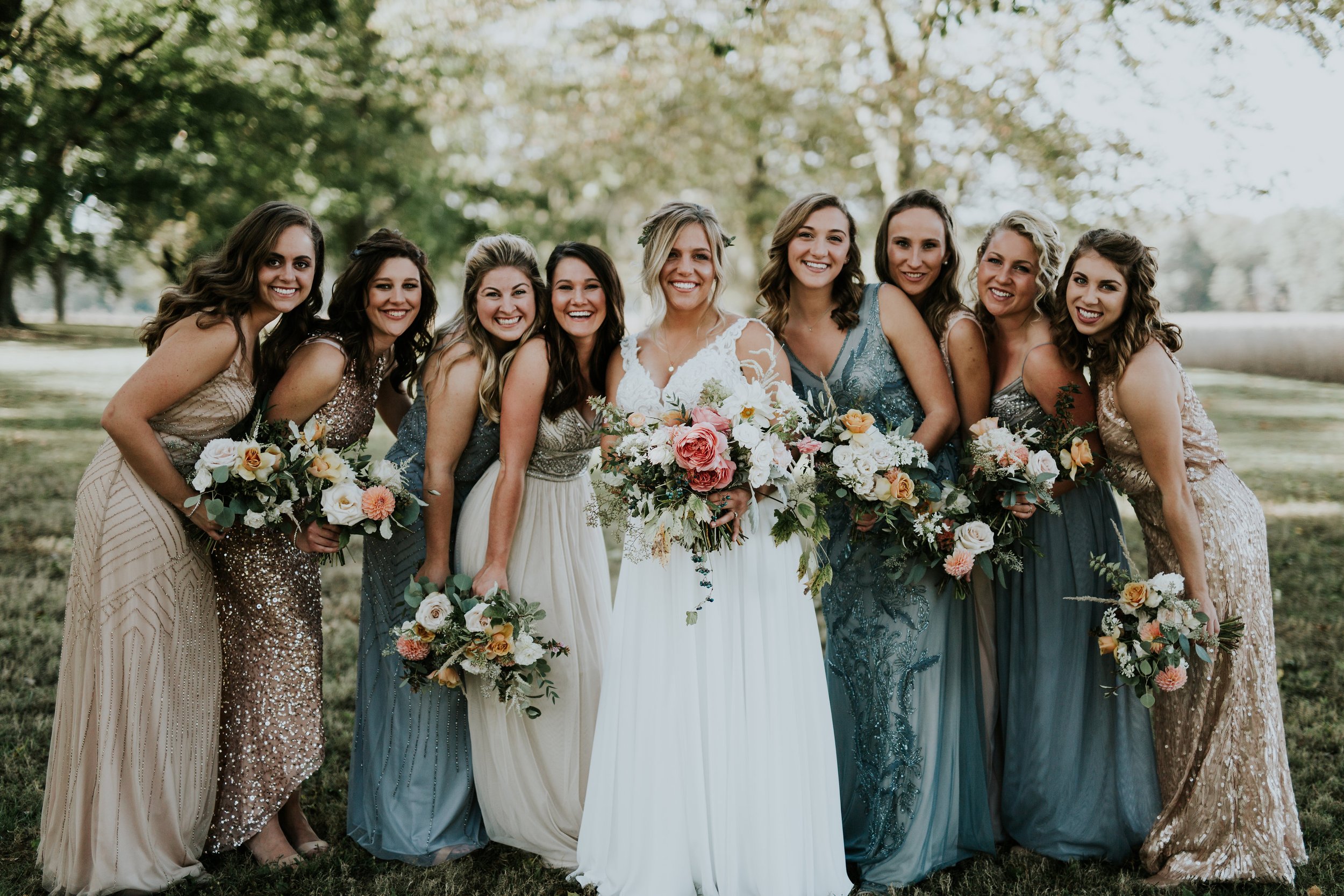 A group of women in colorful dresses holding bouquets, smiling and posing outdoors on a sunny day – styled by One Salon & Bridal Co in St. Charles, IL